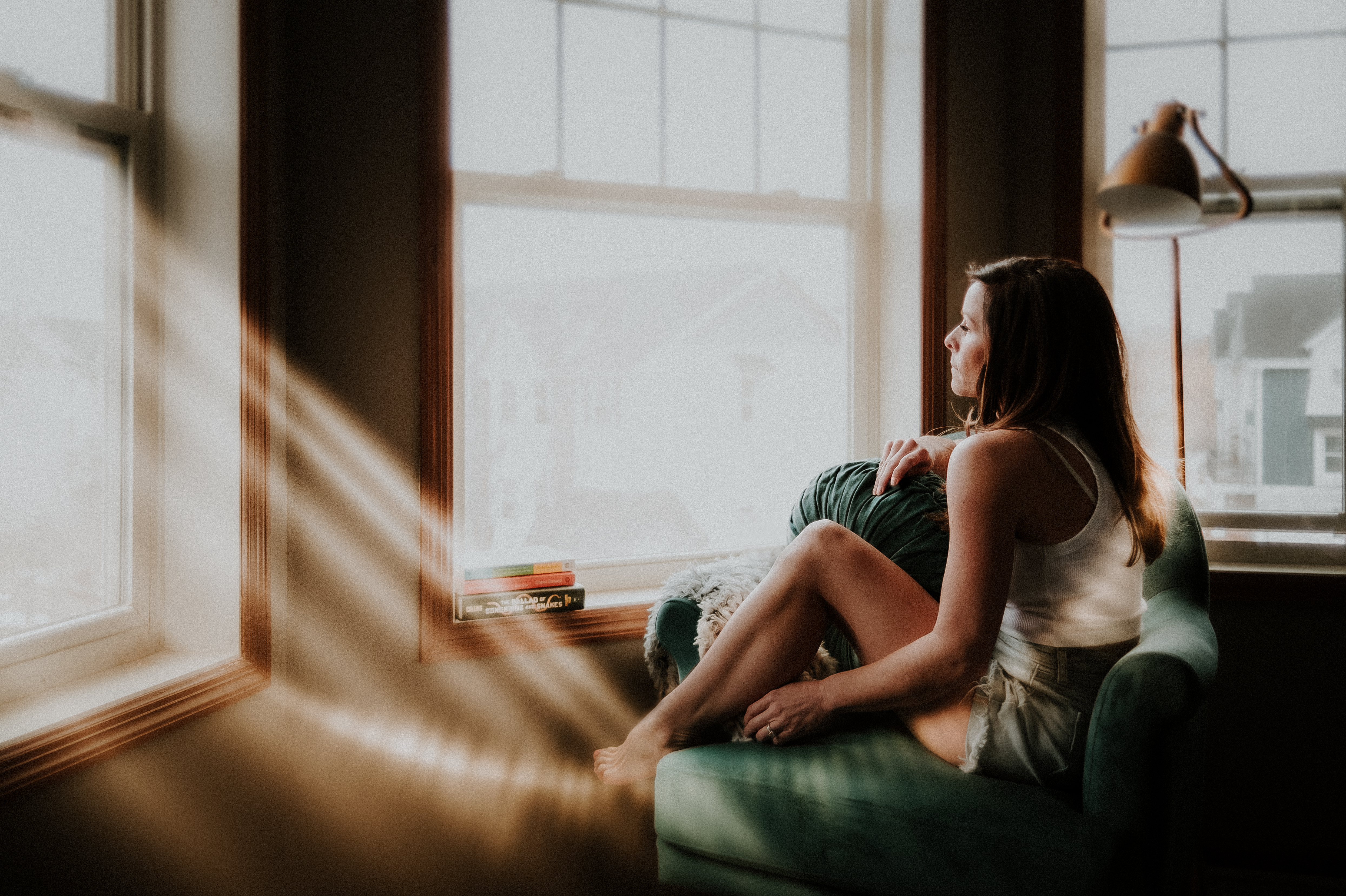 Self-portrait of a woman sitting in a chair looking out the window with an introspective expression, bathed in gorgeous light streaming in through the windows.