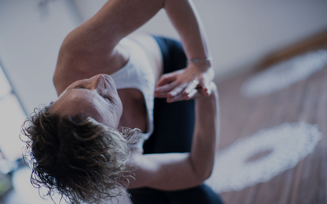 Mujer practica yoga y realiza una torsión con los ojos cerrados, en una postura de torsión y desintoxicación.