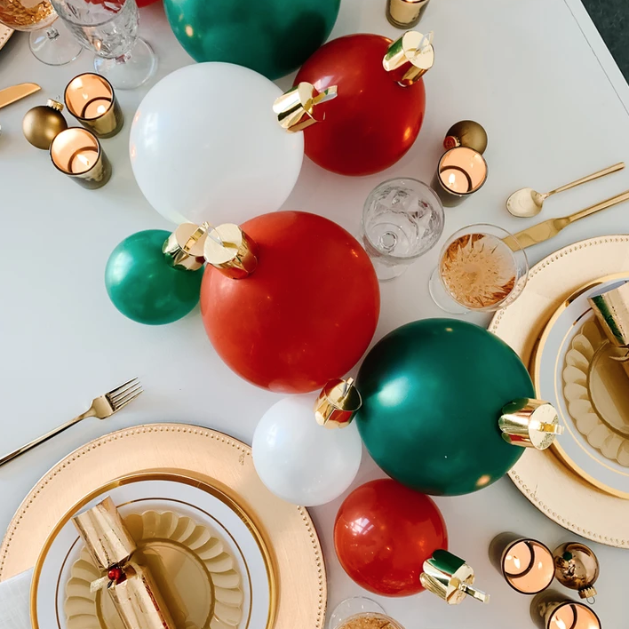 White table with large green, red, and white ornaments and gold place settings