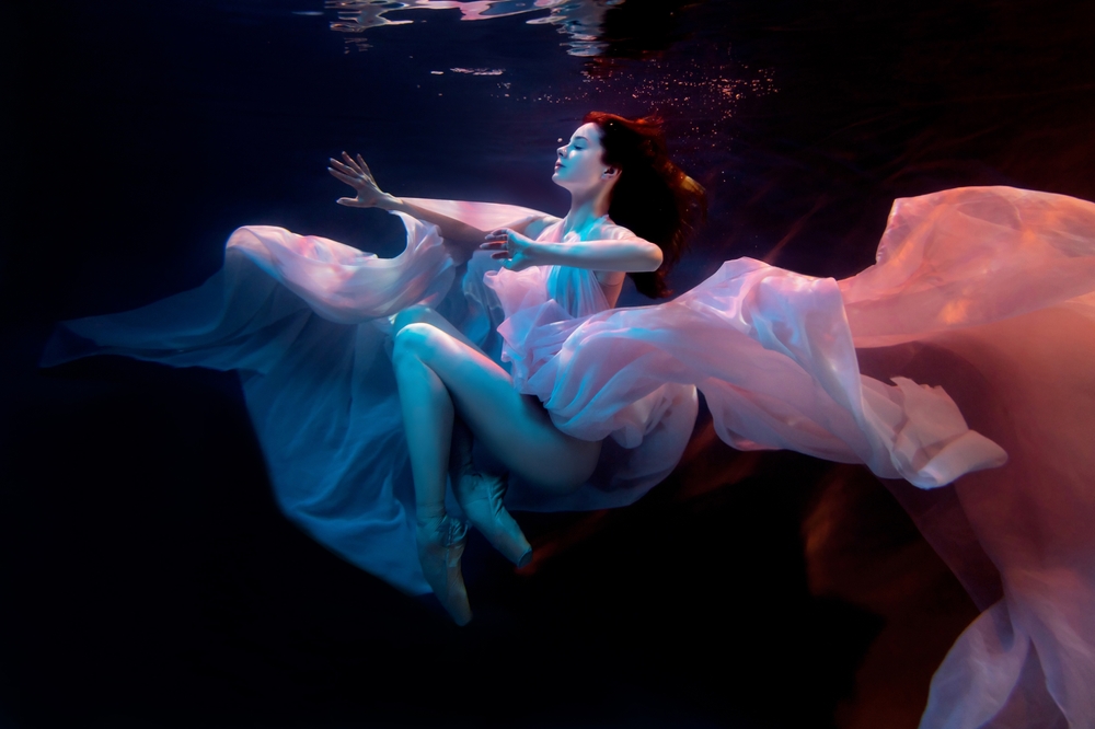 Woman in light gossamer clothing jumping into a pool of water.