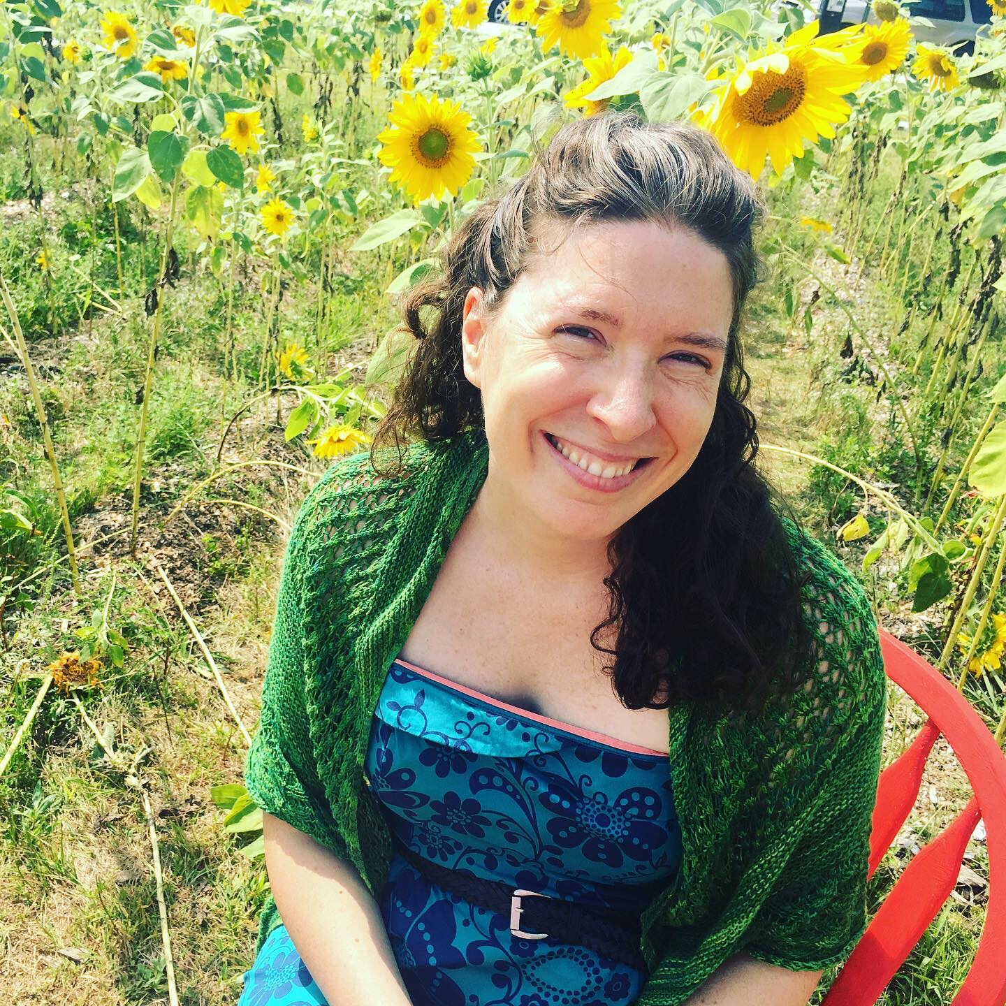 Woman sitting in a red chair in front of a field of sunflowers.