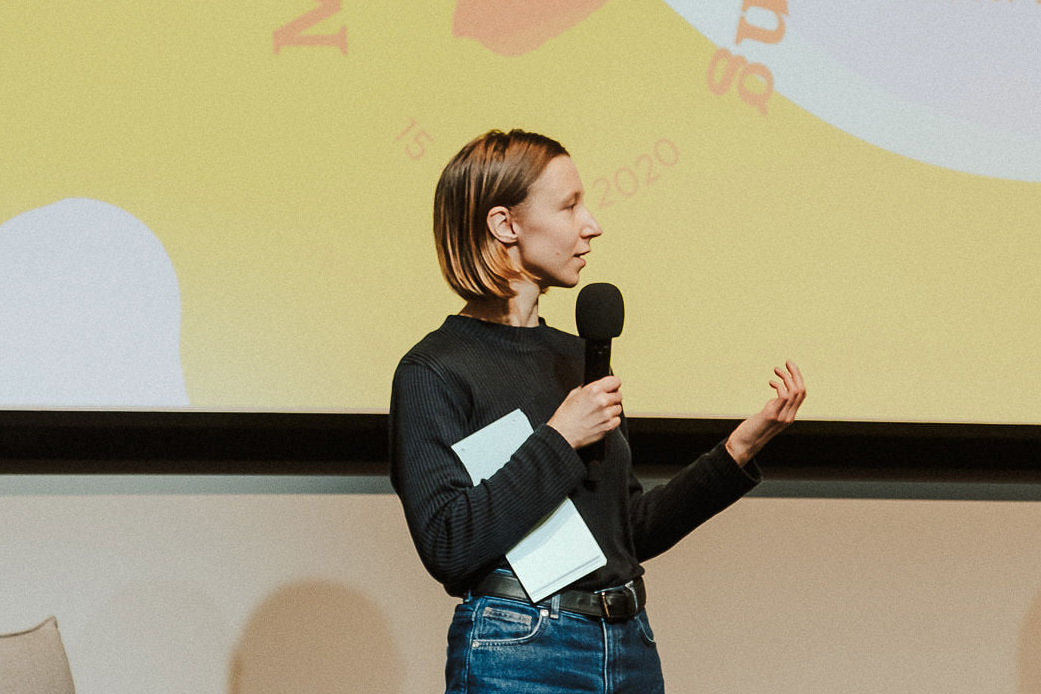 Frau mit schwarzem Oberteil steht auf der Fashion Changers Konferenzbühne und erklärt, wie Lieferketten kreislauffähiger werden können