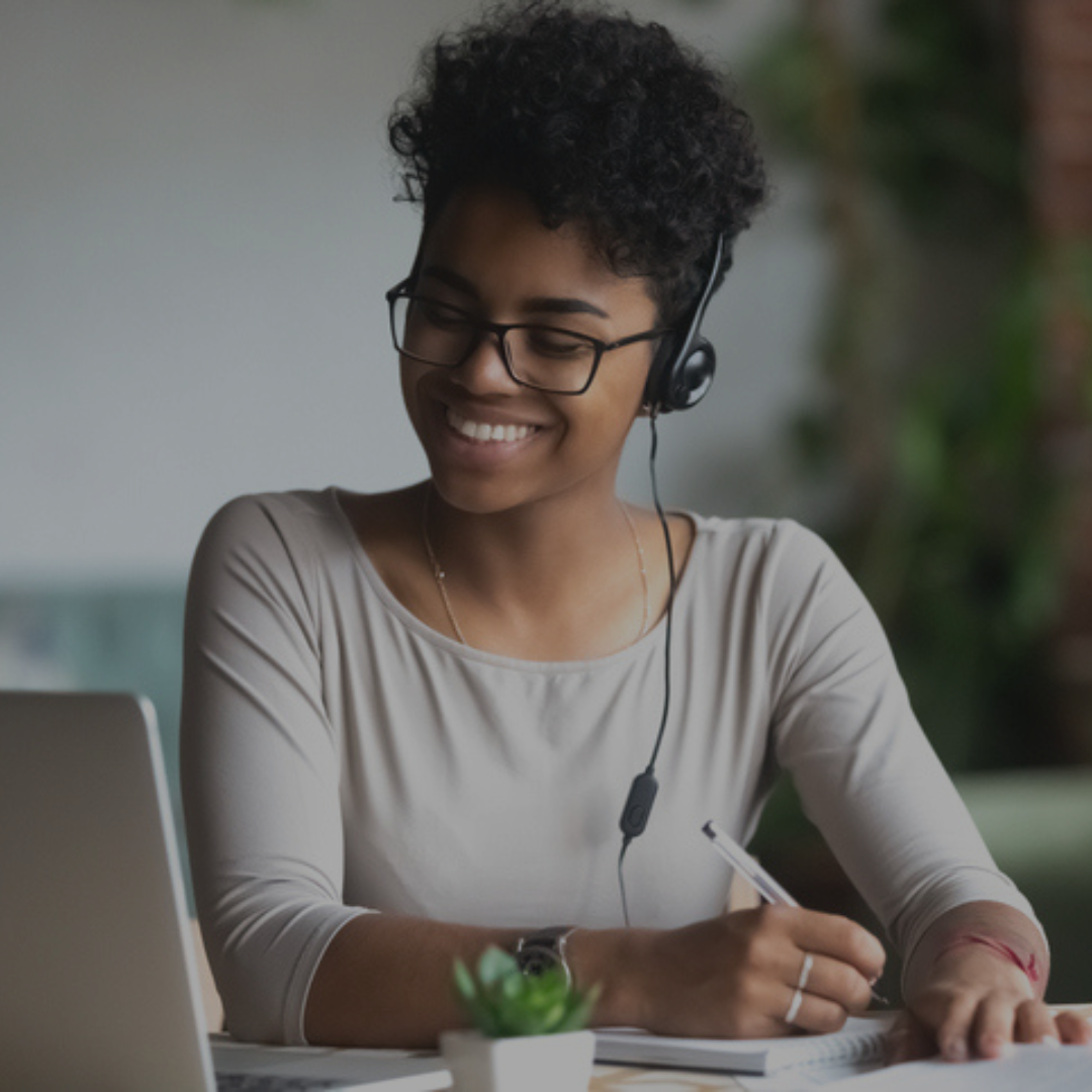 Smiling black woman wearing a headset looks at a laptop