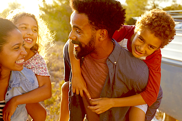 Man and woman smiling at each other whilst giving piggy-back rides to two children