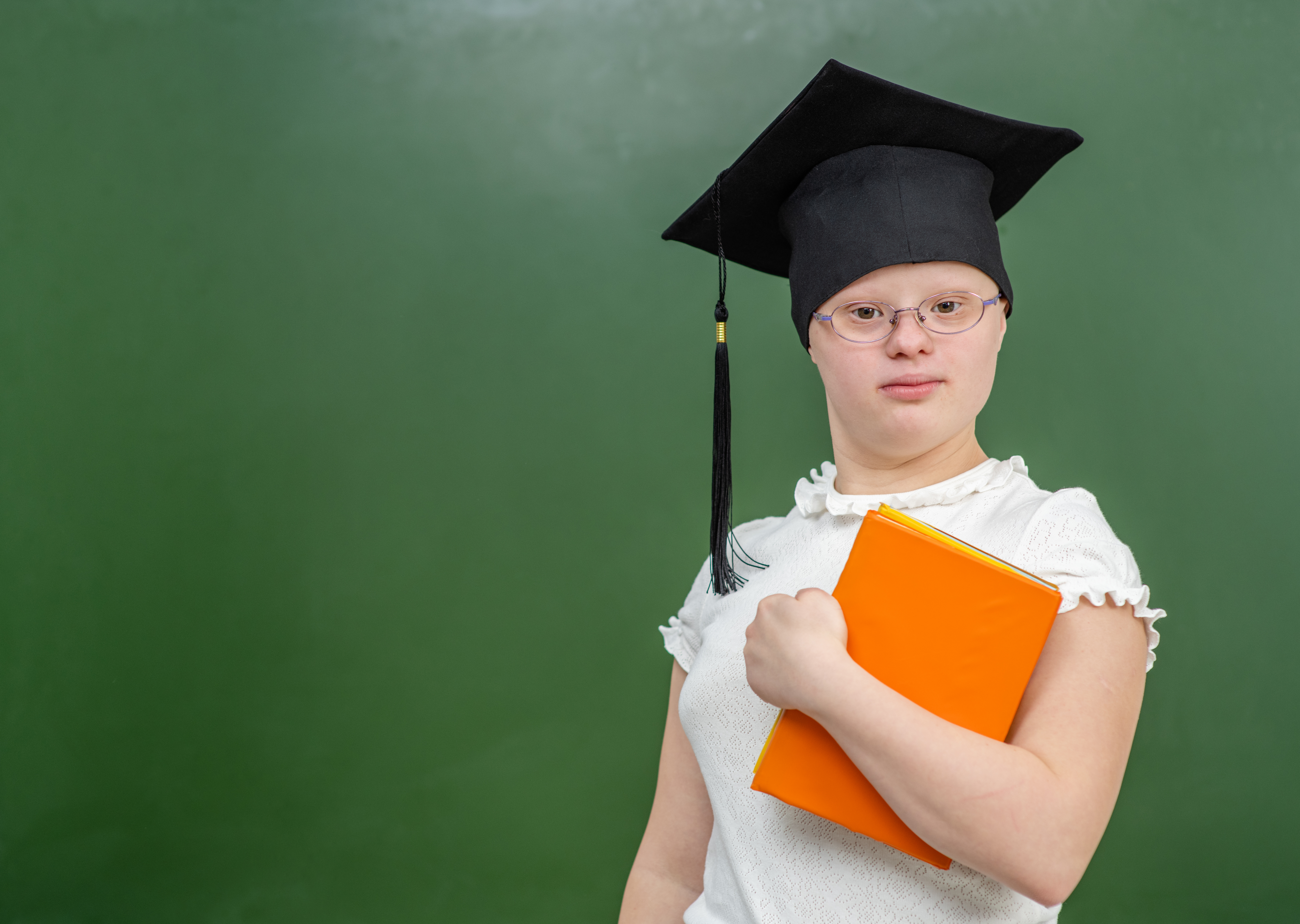 Student wearing a graduation cap and holding an orange book