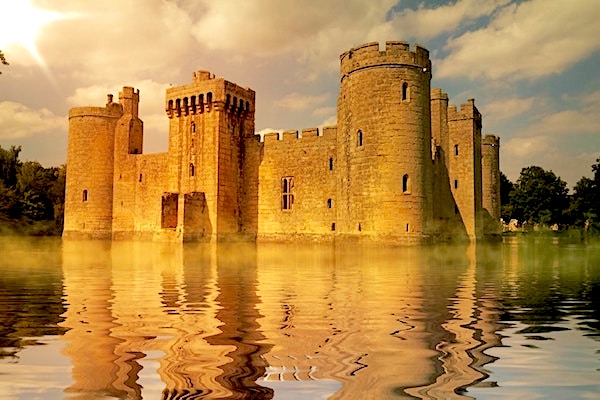 Old golden stone castle with a large moat of water in front of it