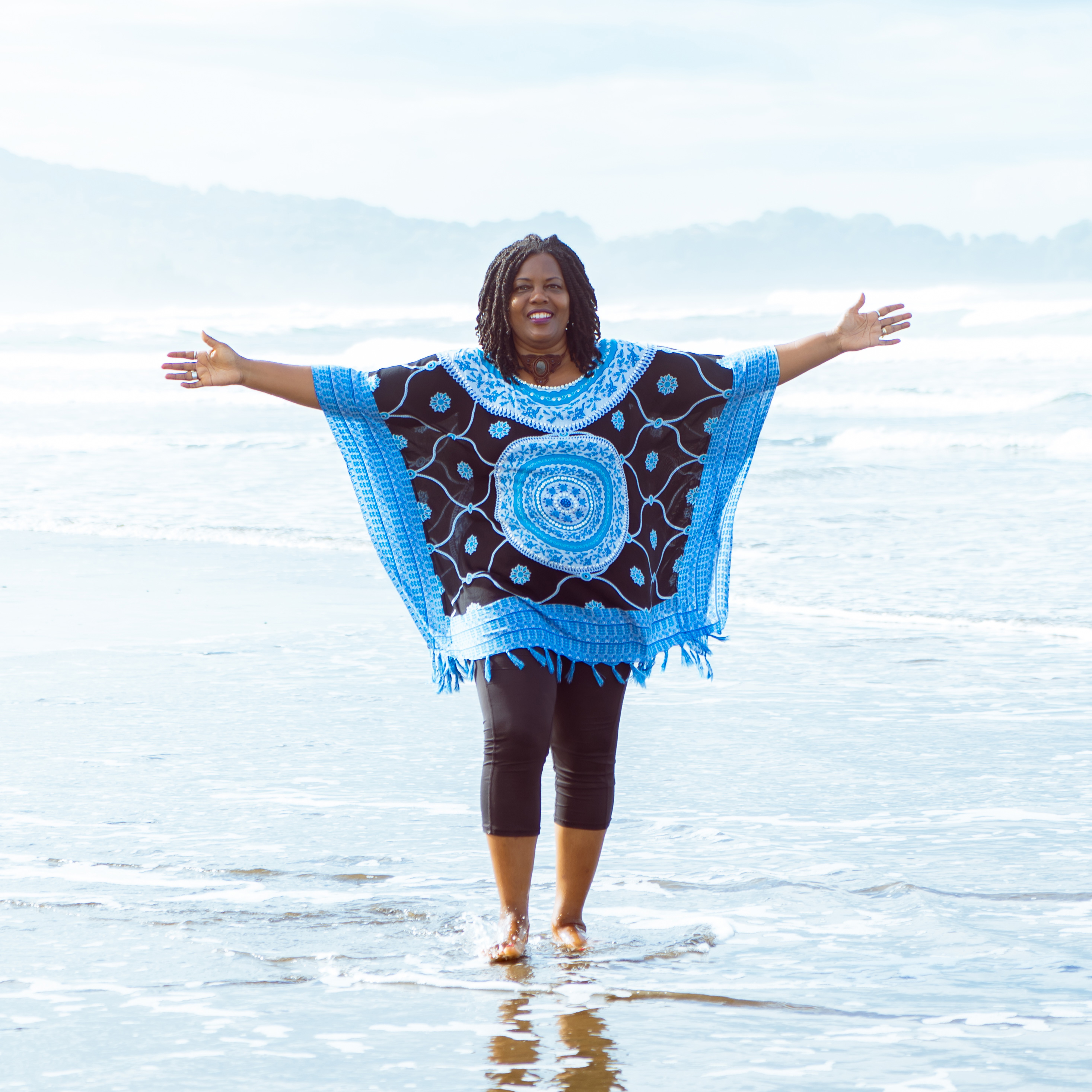 Photo of Dawn James standing on a beach and smiling, with her arms wide open