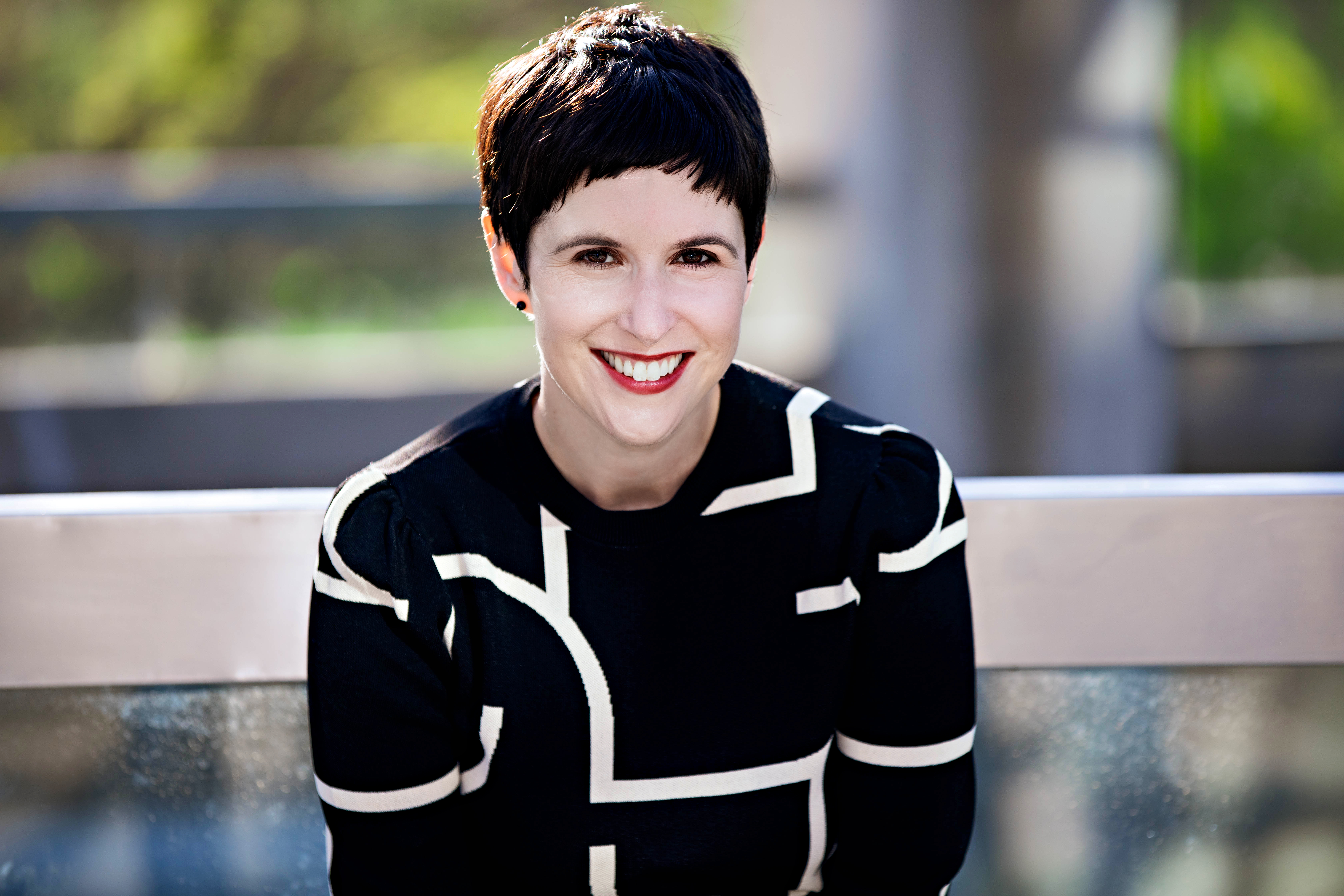 Laura Portwood-Stacer, photographed from the elbows up, smiling widely for the camera