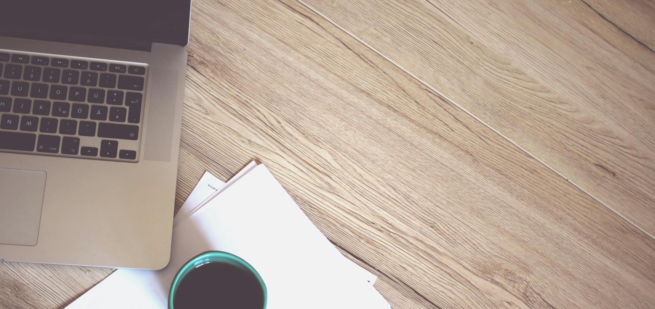 A wooden desk with a laptop and coffee cup setup for online learning.