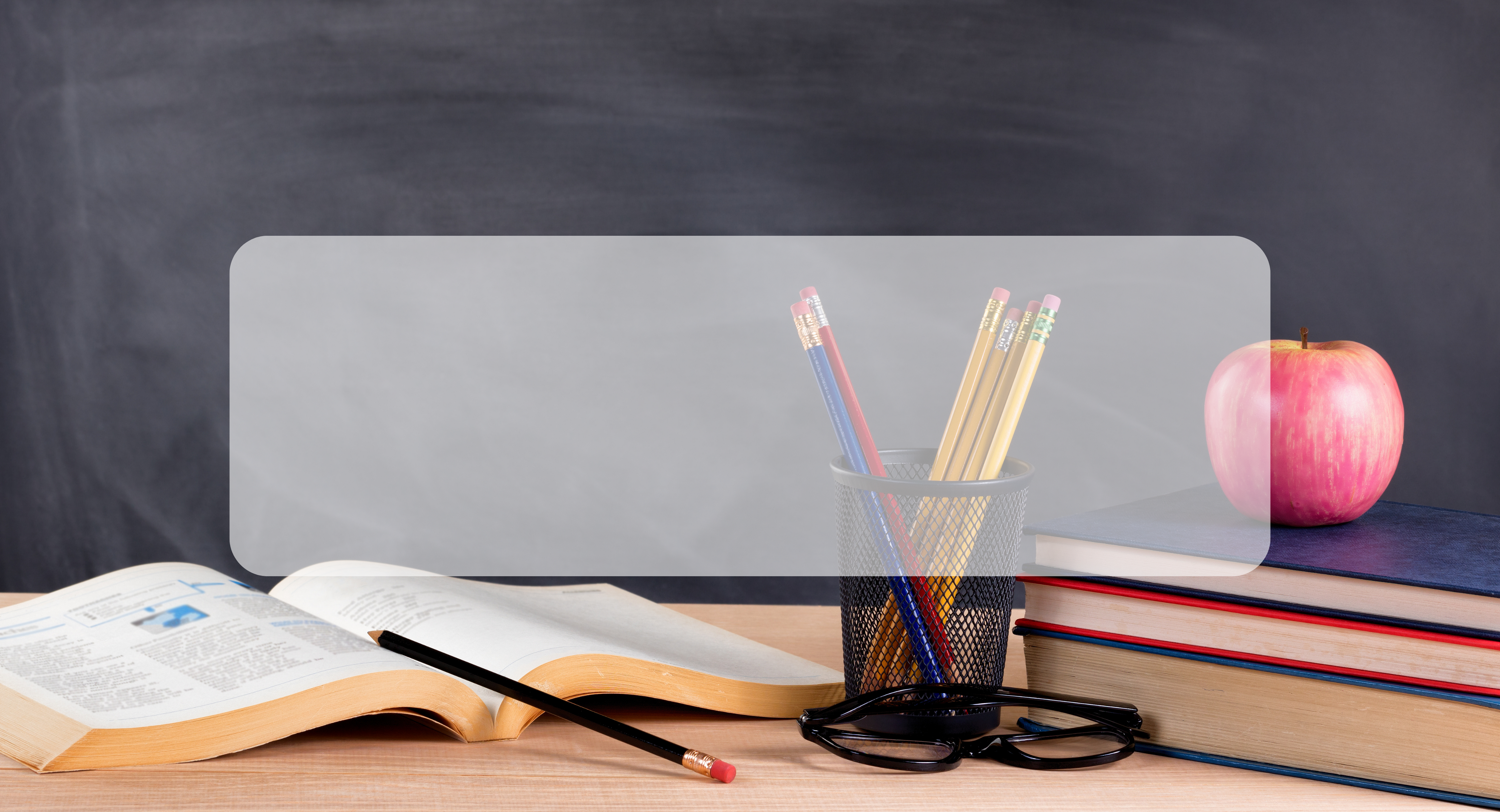 chalkboard in background, book, pencils, and apple on desk