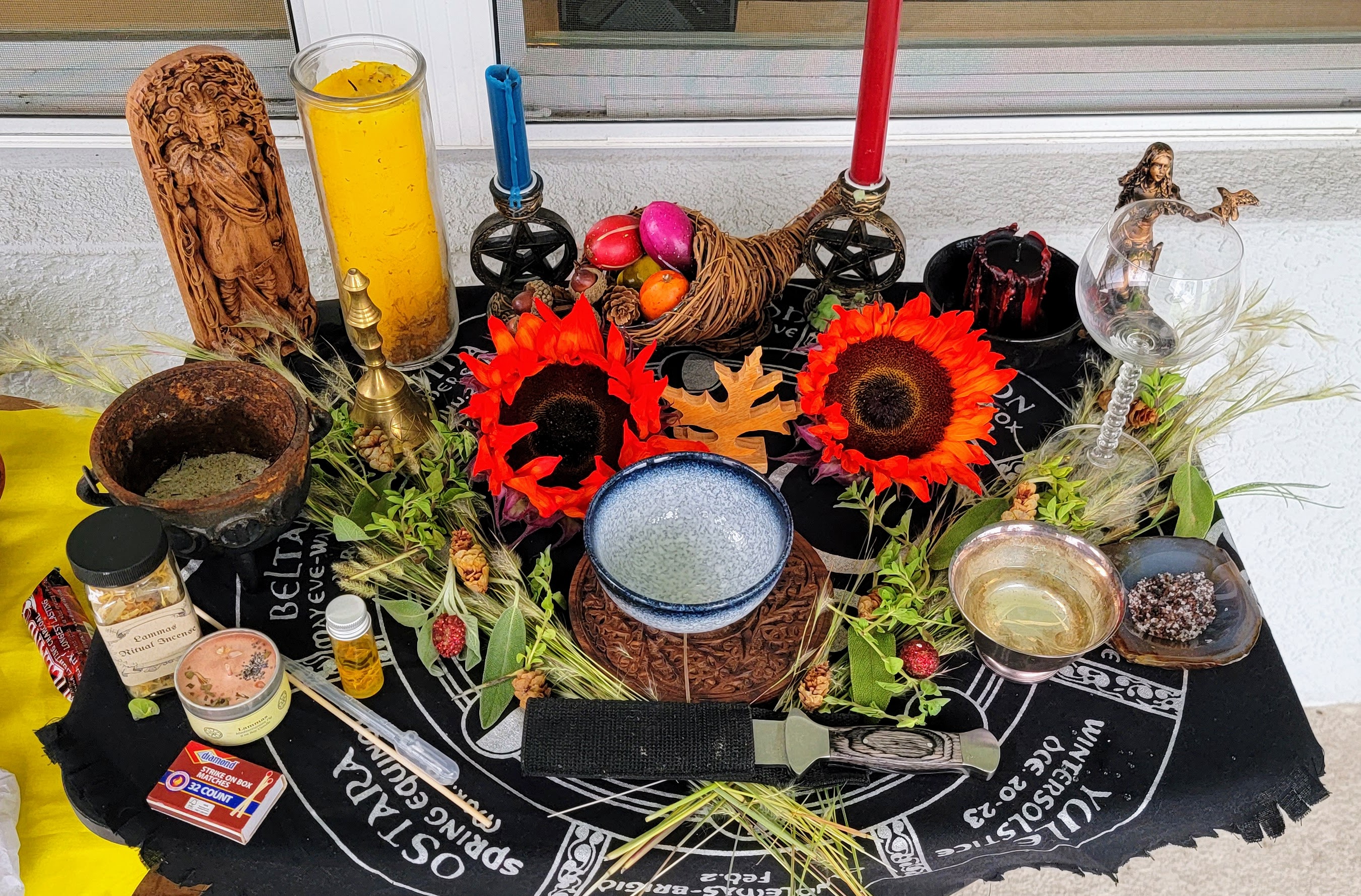 A brightly colored wiccan Altar arragement covered with fresh sunflowers, incense, statues and candles