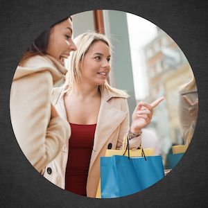 two smiling friends holding shopping bags are looking and pointing in shop window