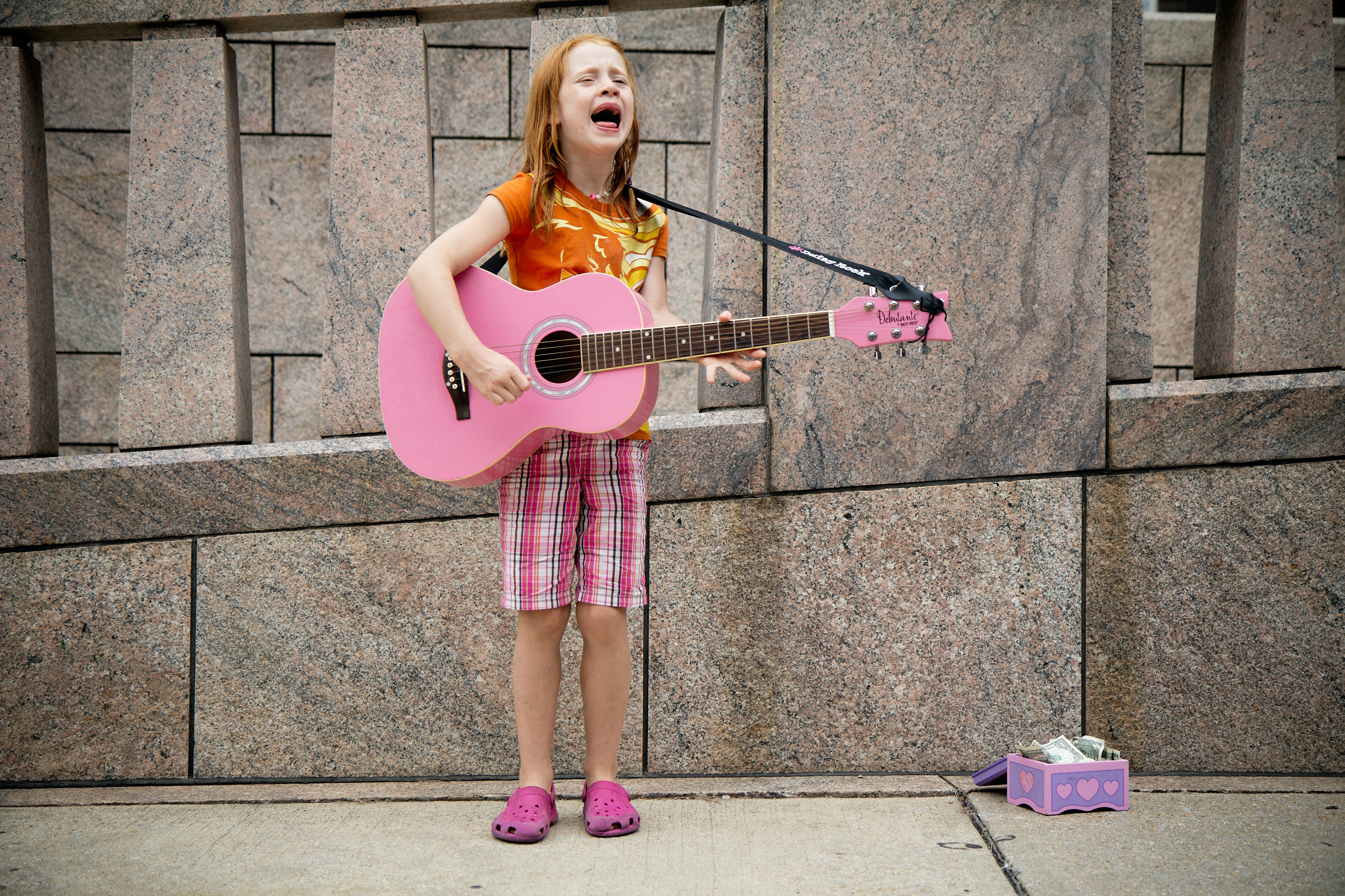 Child holding pink guitar on street
