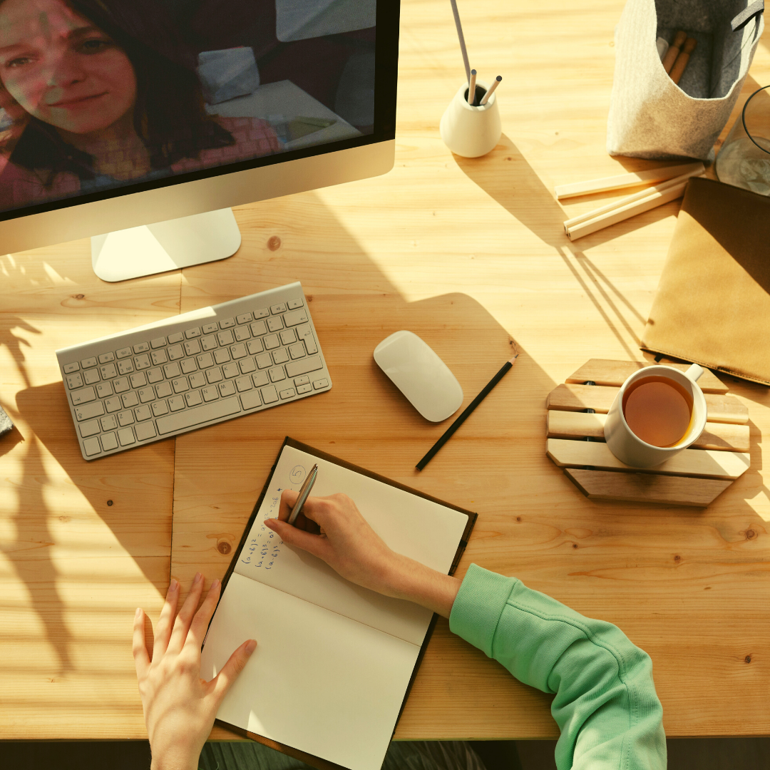 Top-down view of a person looking at a computer and writing in a notebook