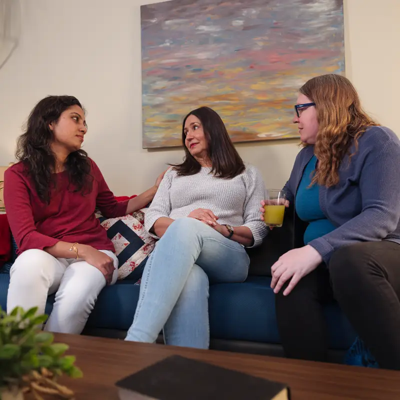 Une personne en détresse est assise sur un canapé avec deux amies qui la réconfortent.