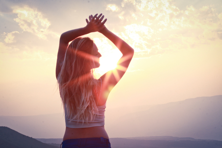 Blonde woman stretching arms up and turning head away from the sun