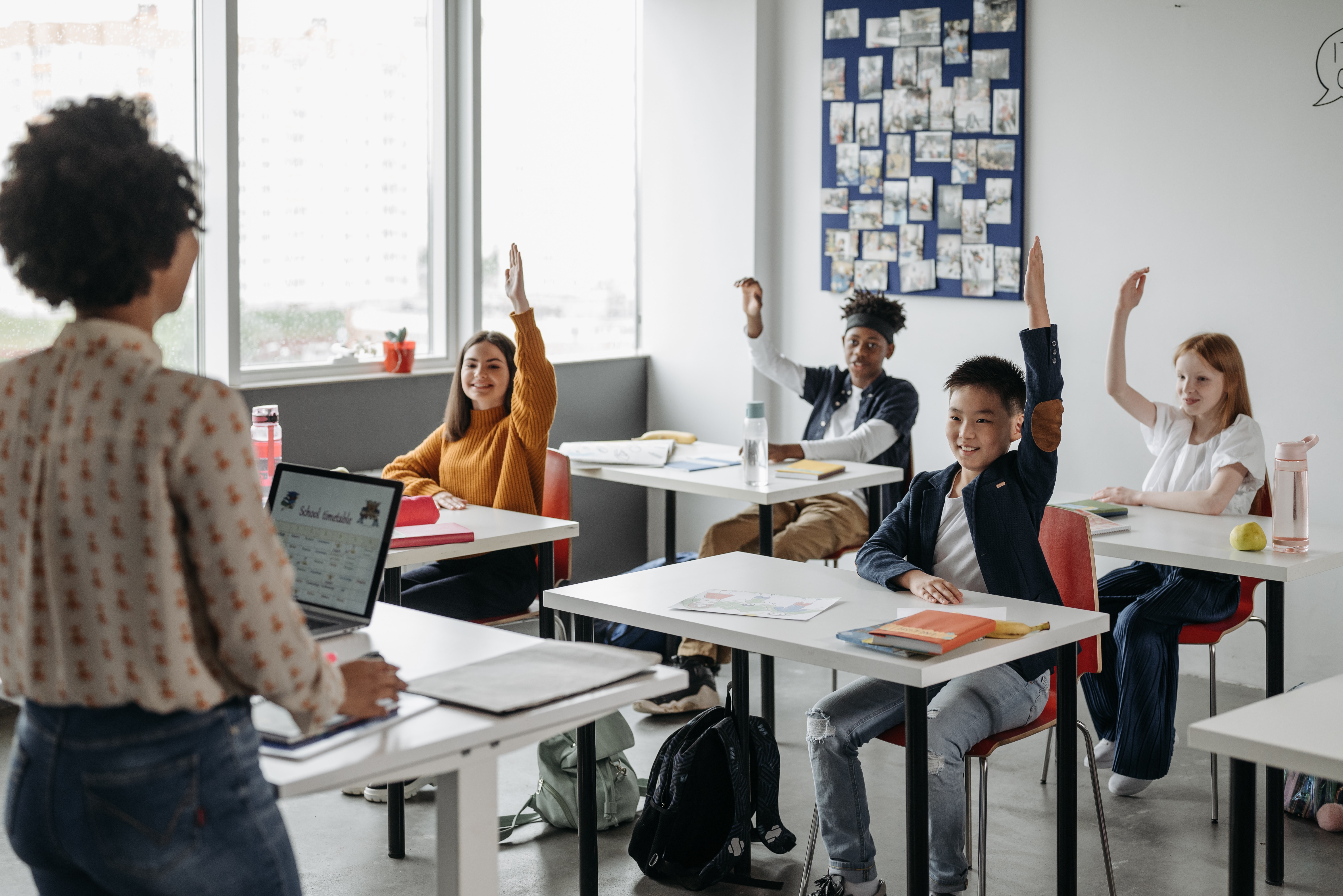 teacher in front of class, students raising hands