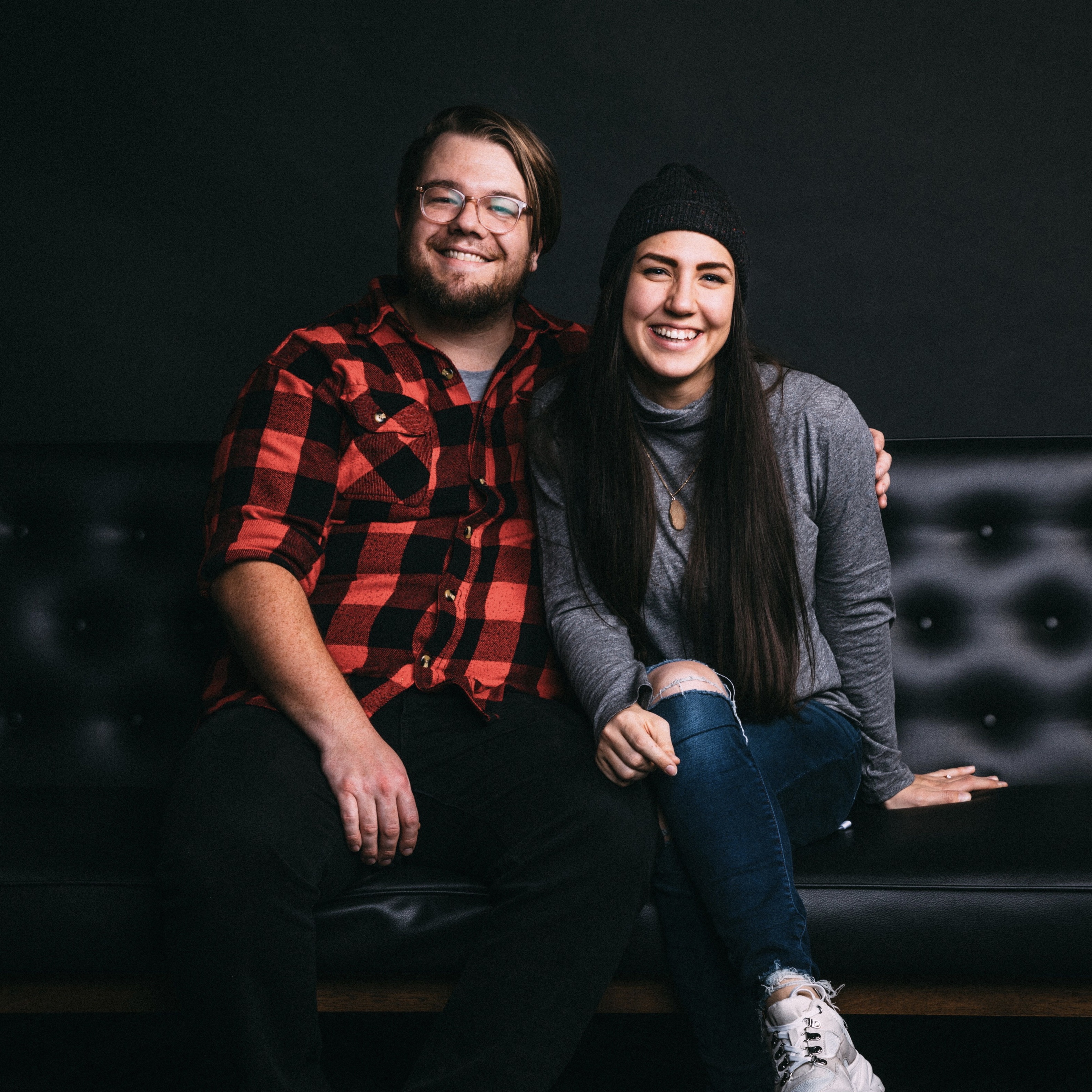 A young couple sit together on a black leather sofa