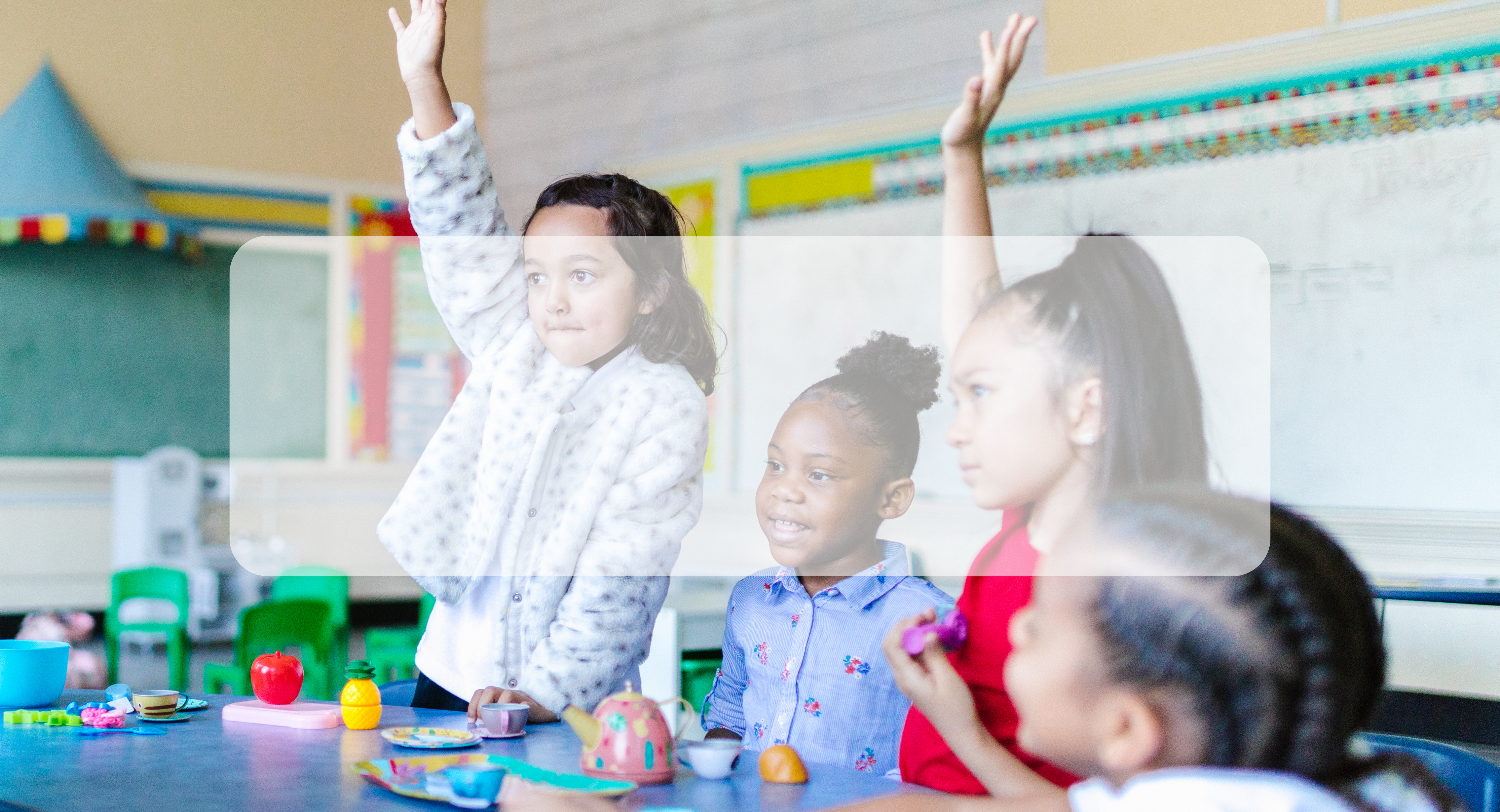 students raising hands at table in classroom