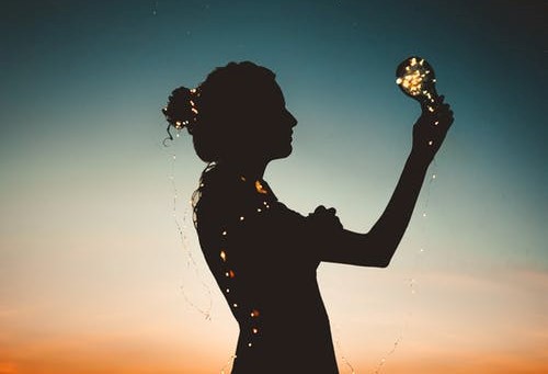 pink/blue sunset with silhouette lady holding light bulb and fairy lights