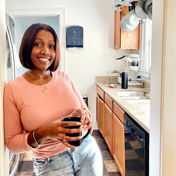 black woman leaning on wall in pink shirt drinking coffee from black mug