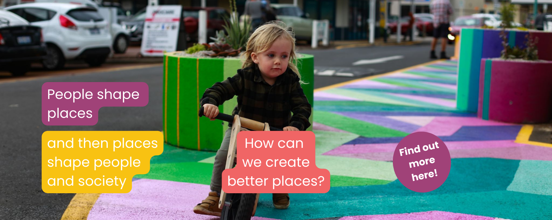 Placemaking. People shape place and then places shape people and society. How can we create better places? Find out more here. The image show a small boy riding a small bicycle on a roadway painted in bright colours with painted concrete planters in the background.