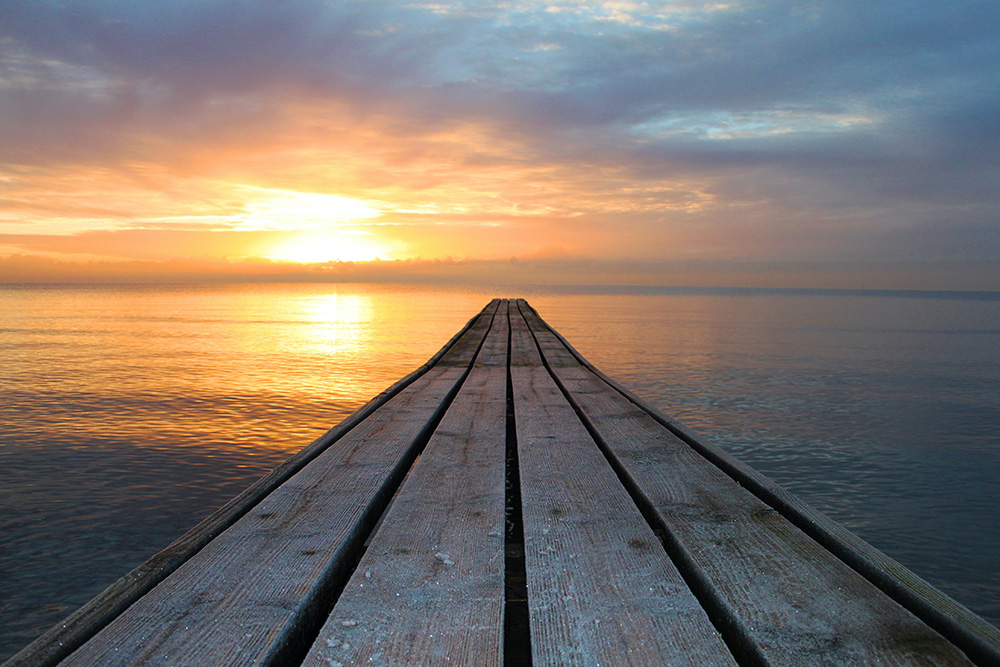 A jetty reaching over water towards the sunset