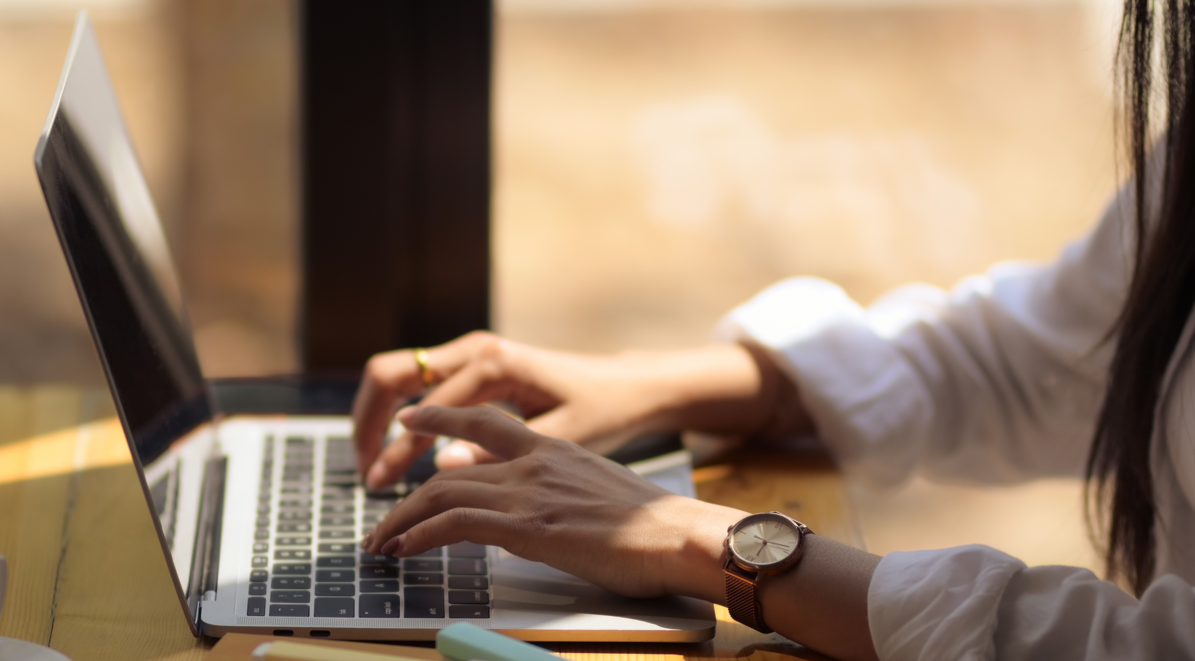 A laptop is open on a desk in front of an open cube bookshelf. We see hands typing but the screen is away from us.