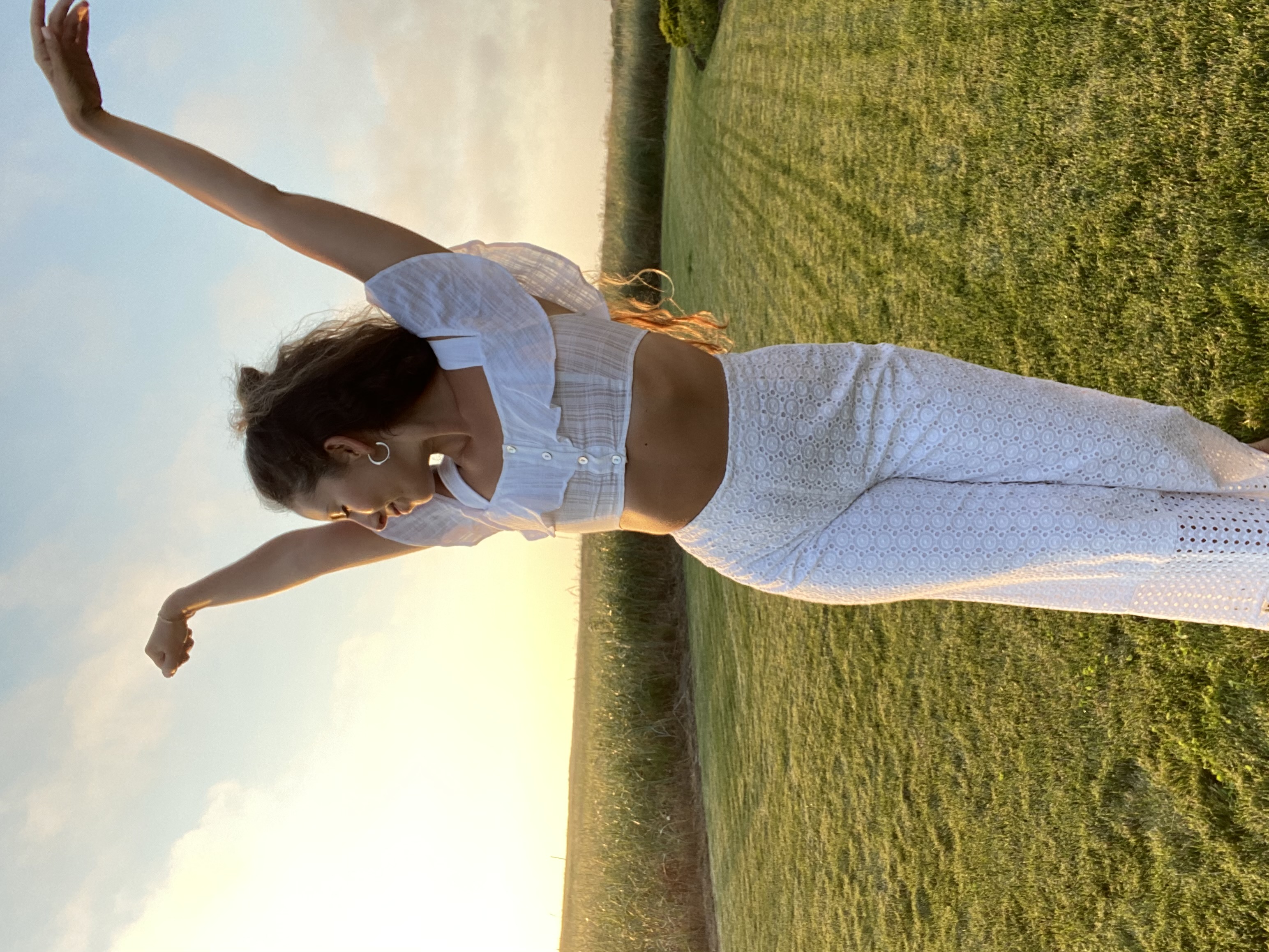 woman feeling happy and free in a white crop top and high waisted pants in a field of grass