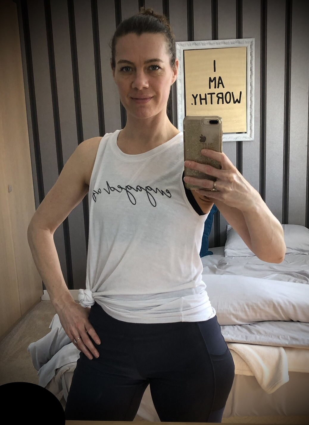 Woman standing taking a selfie with a tank top that says engaged af and a sign behind her saying I am worthy.