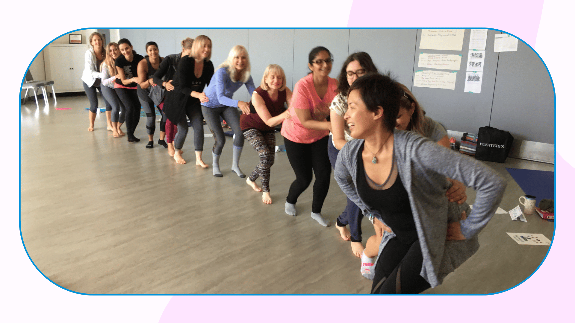 a group of 12 stand and form a yoga train by holding each other by the hips or shoulders and travel throug the open floor in front of the leader