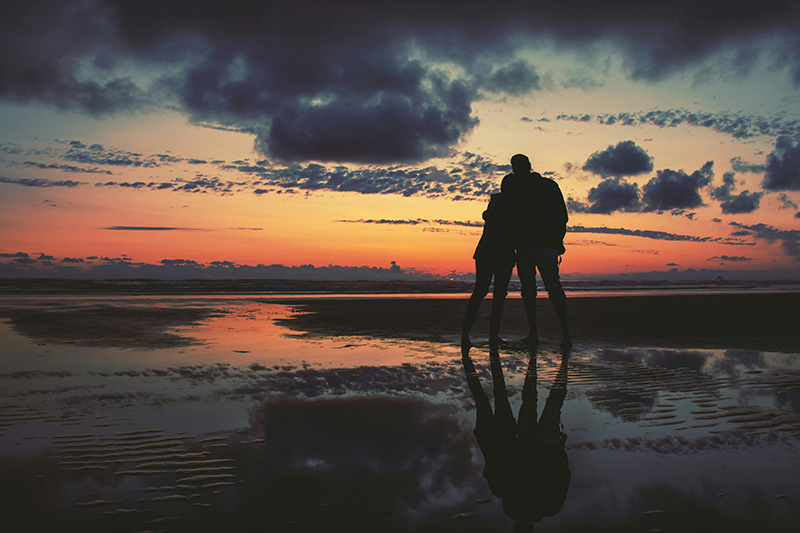 A couple standing on a beach at sunset under grey clouds