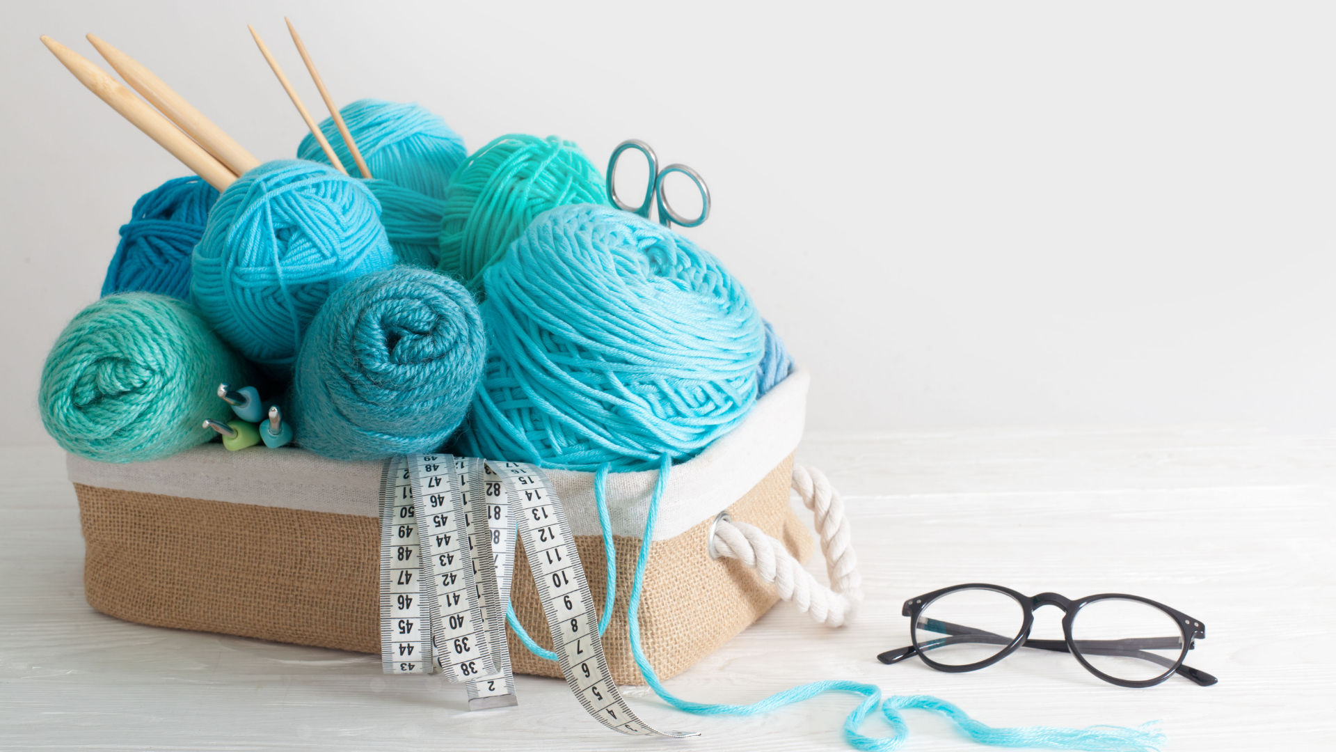 yarn in a basket with tape measure knitting needles and glasses