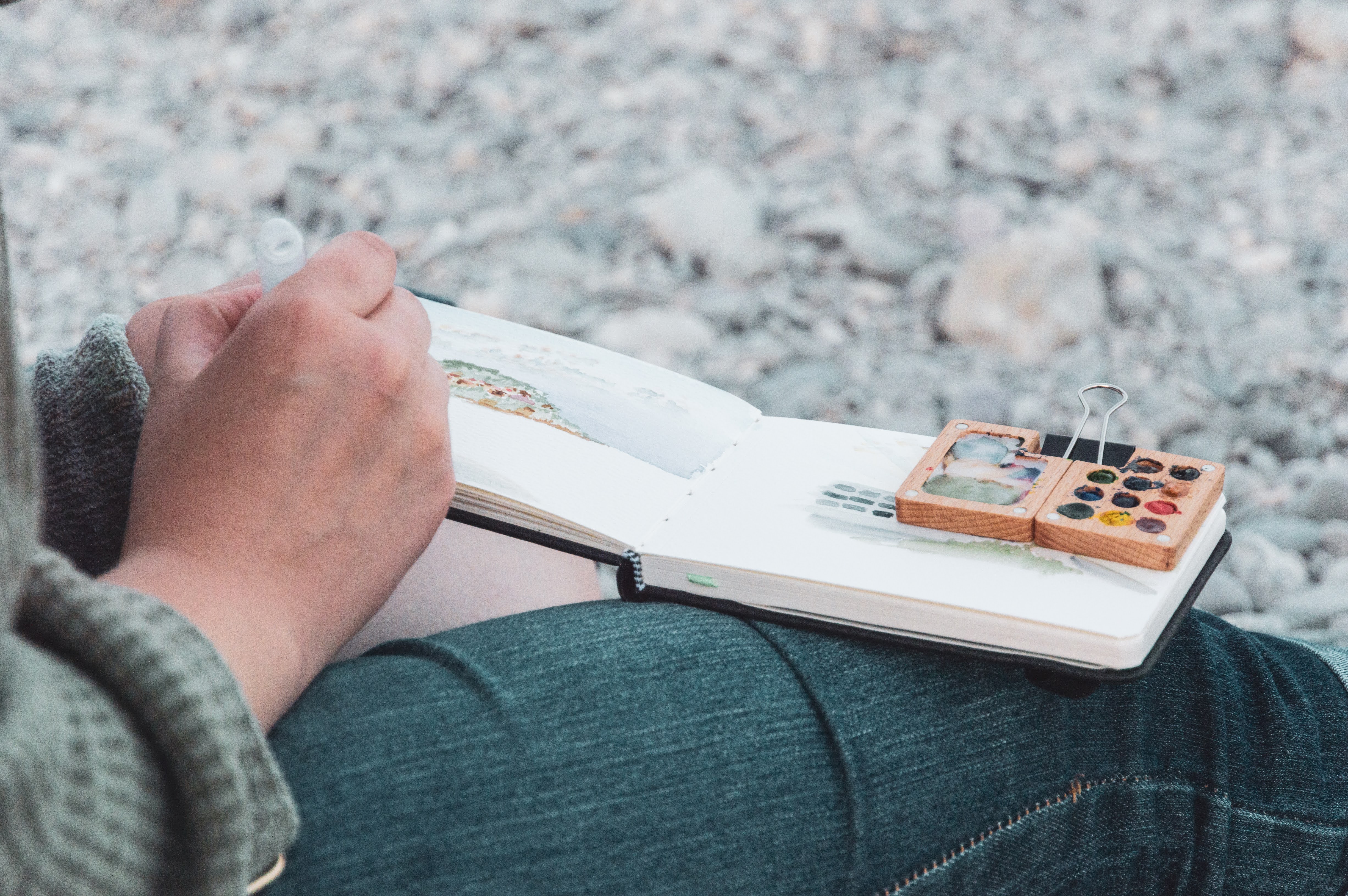 painting in a sketchbook on a rocky beach