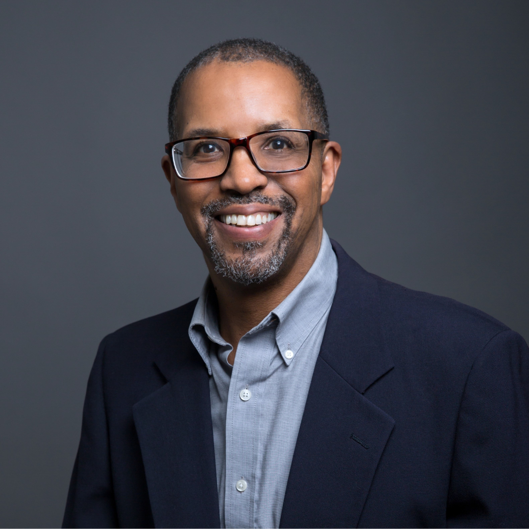 Anthony Peterson in a suit jacket and glasses on a gray backdrop