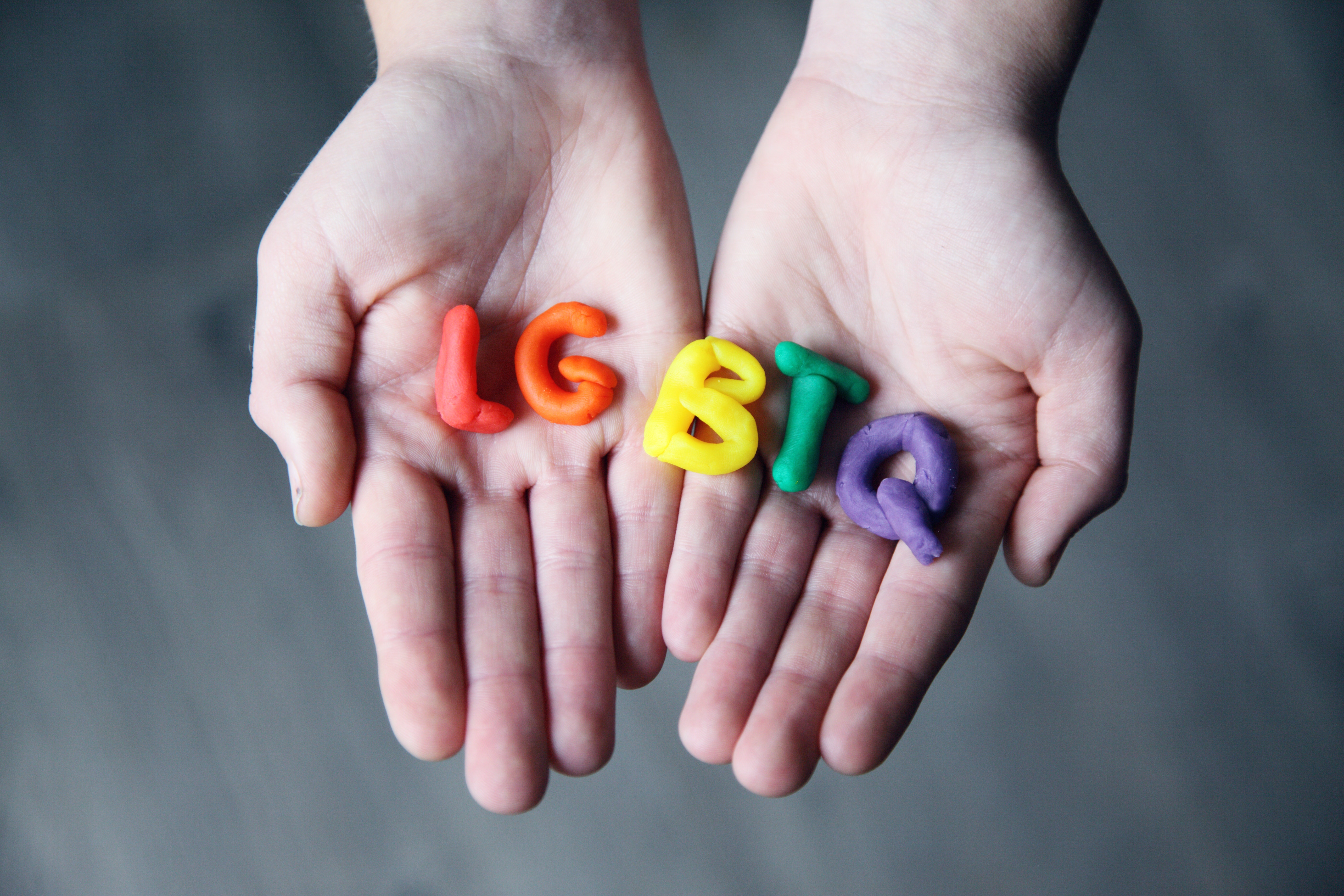 Two hands holding play dough in the shape of the letters L, G, B, T, and Q.