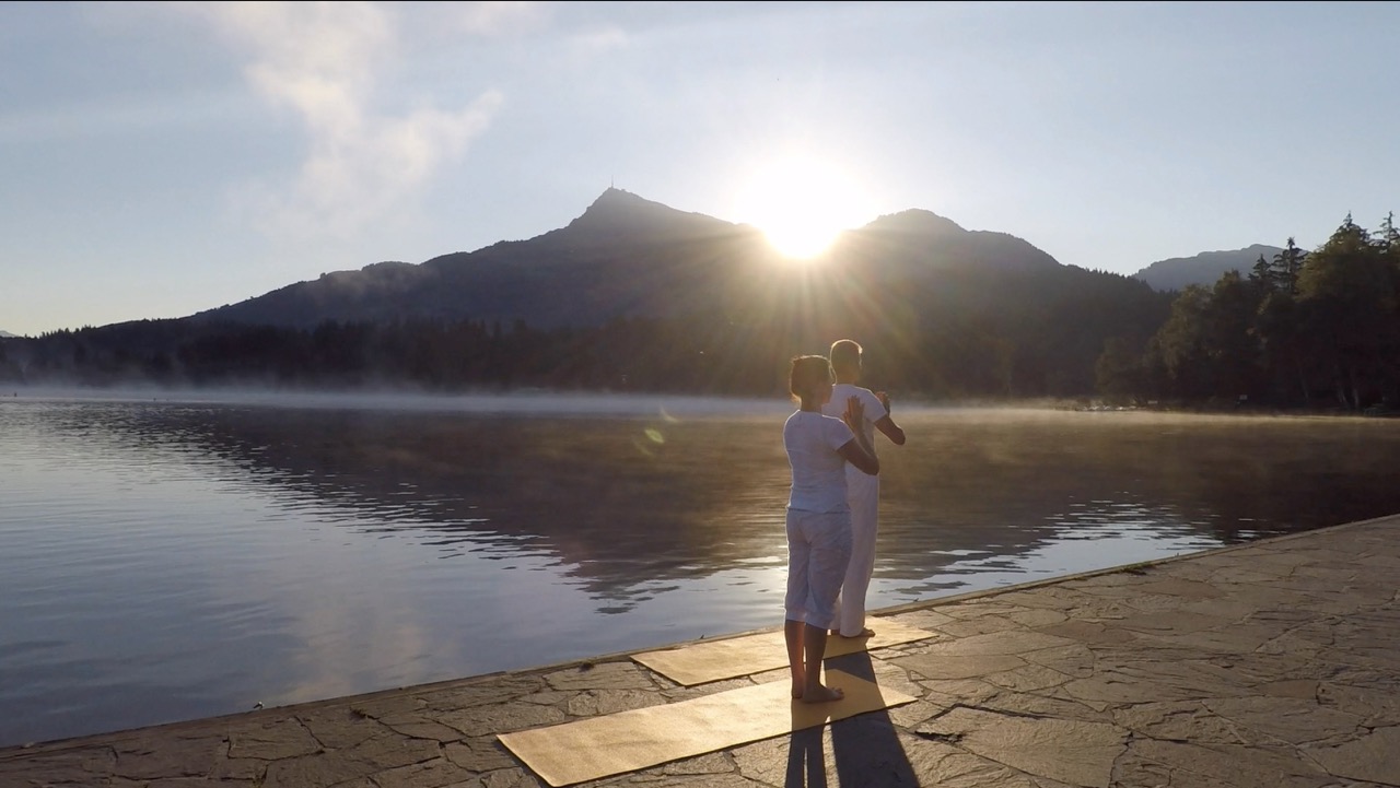 two people doing surya namaskar by the lake when the sun rise up