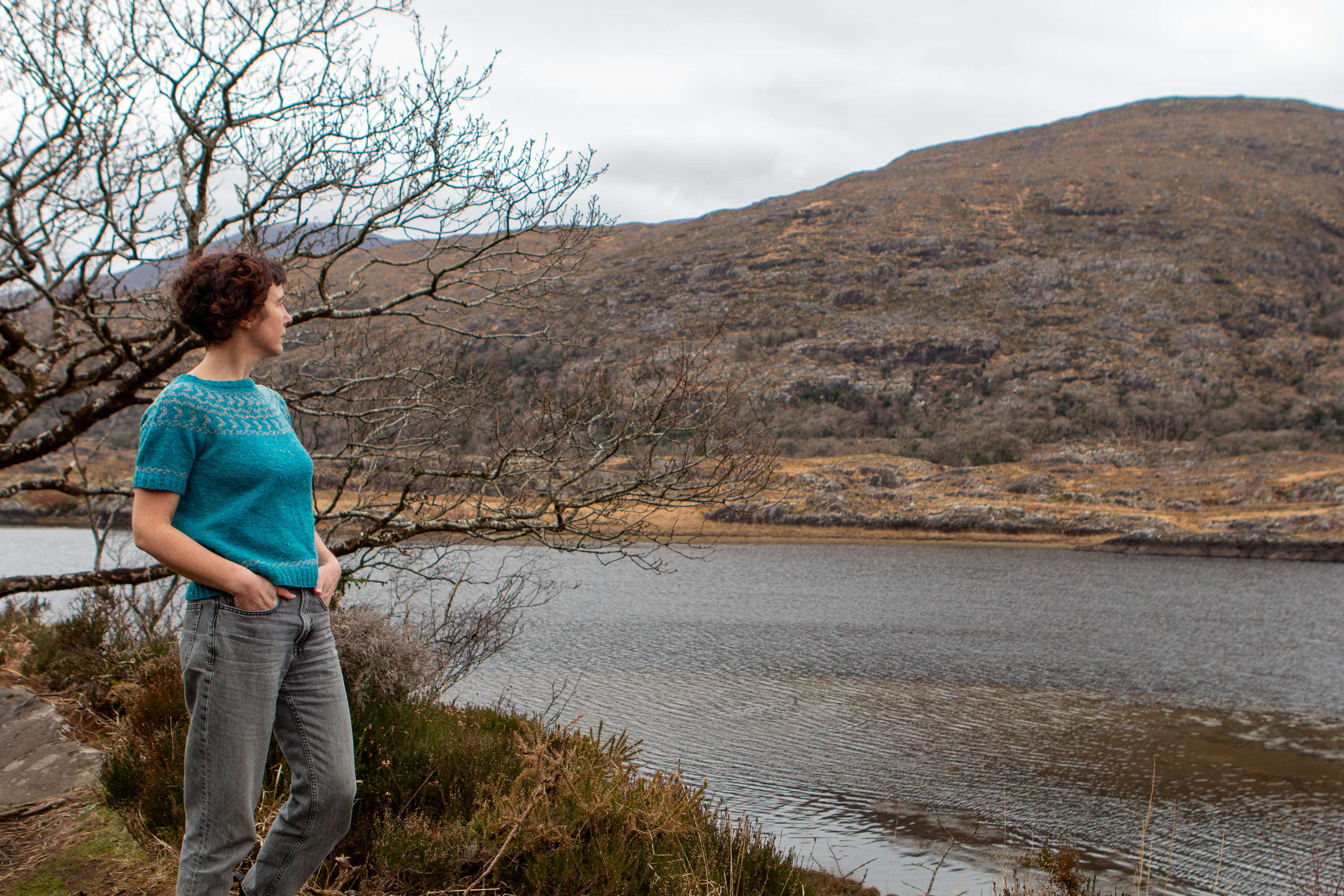 Carol Feller wearing the short sleeved Daingean Sweater while looking out on a beautiful lake and mountain scene. 