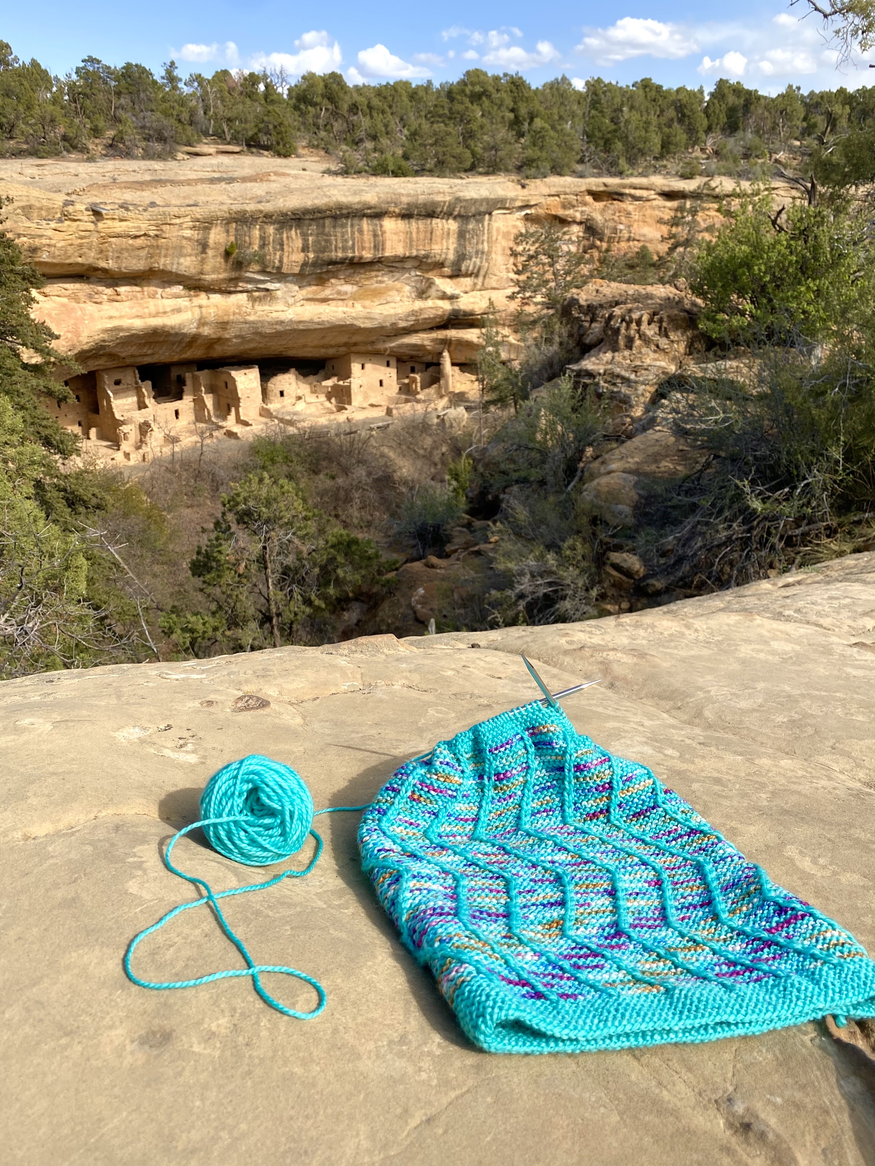 Knitting on needles in front of mesa verde national park dwellings