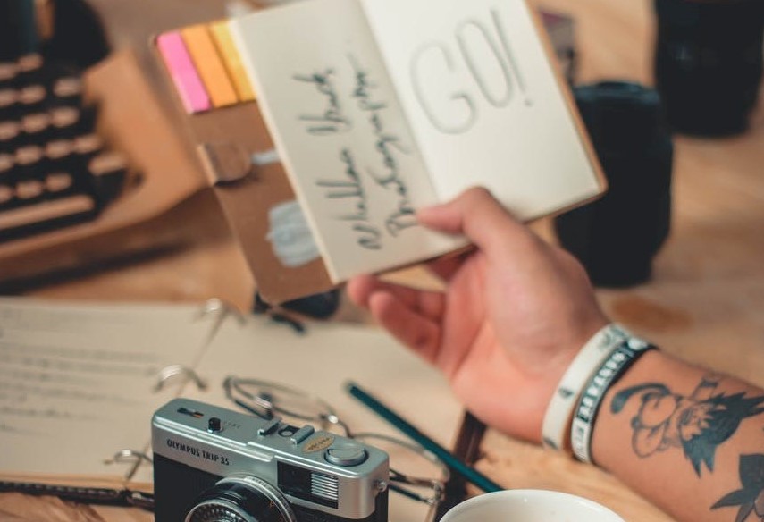 Photo of a tattooed arm, holding a notebook that says GO - Coaching for Creatives