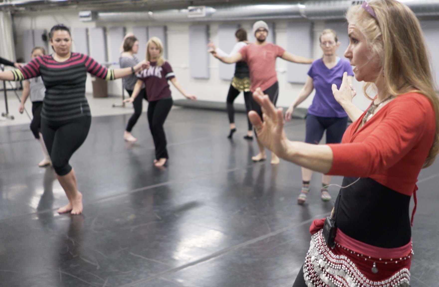 mature senior women wearing hip scarfs learning to belly dance in living room