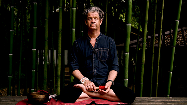 Martin Aylward sitting cross-legged on a platform surrounded by bamboo
