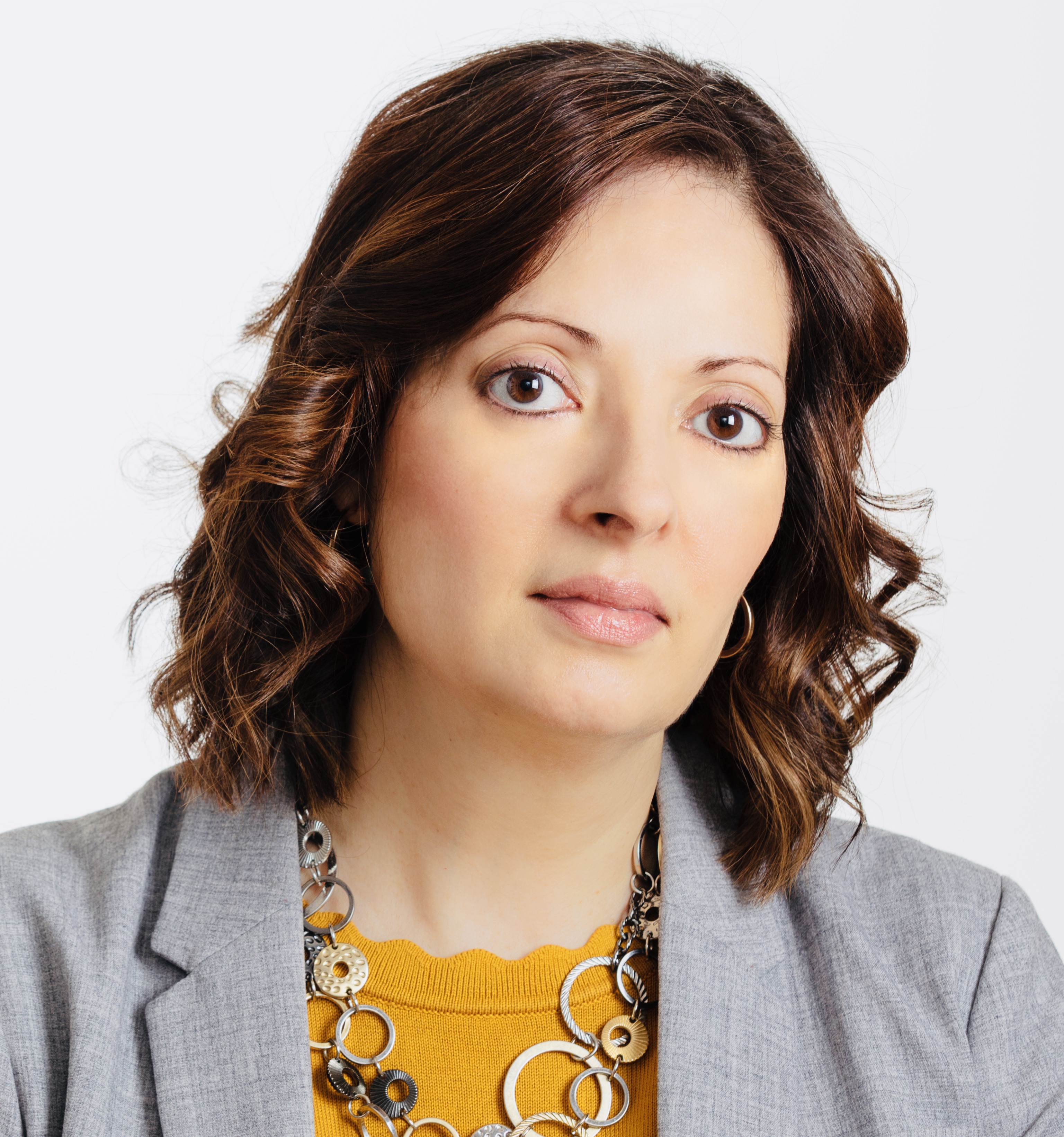 Image of the founding lawyer and educator with an expression of listening attentively. She is wear a grey blazer, mustard sweater with earrings and a necklace.  