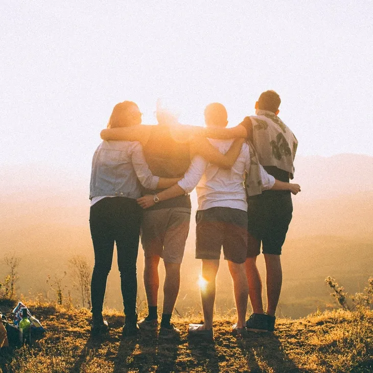 Four people on hilltop overlooking mountains in summer time with arms around each other