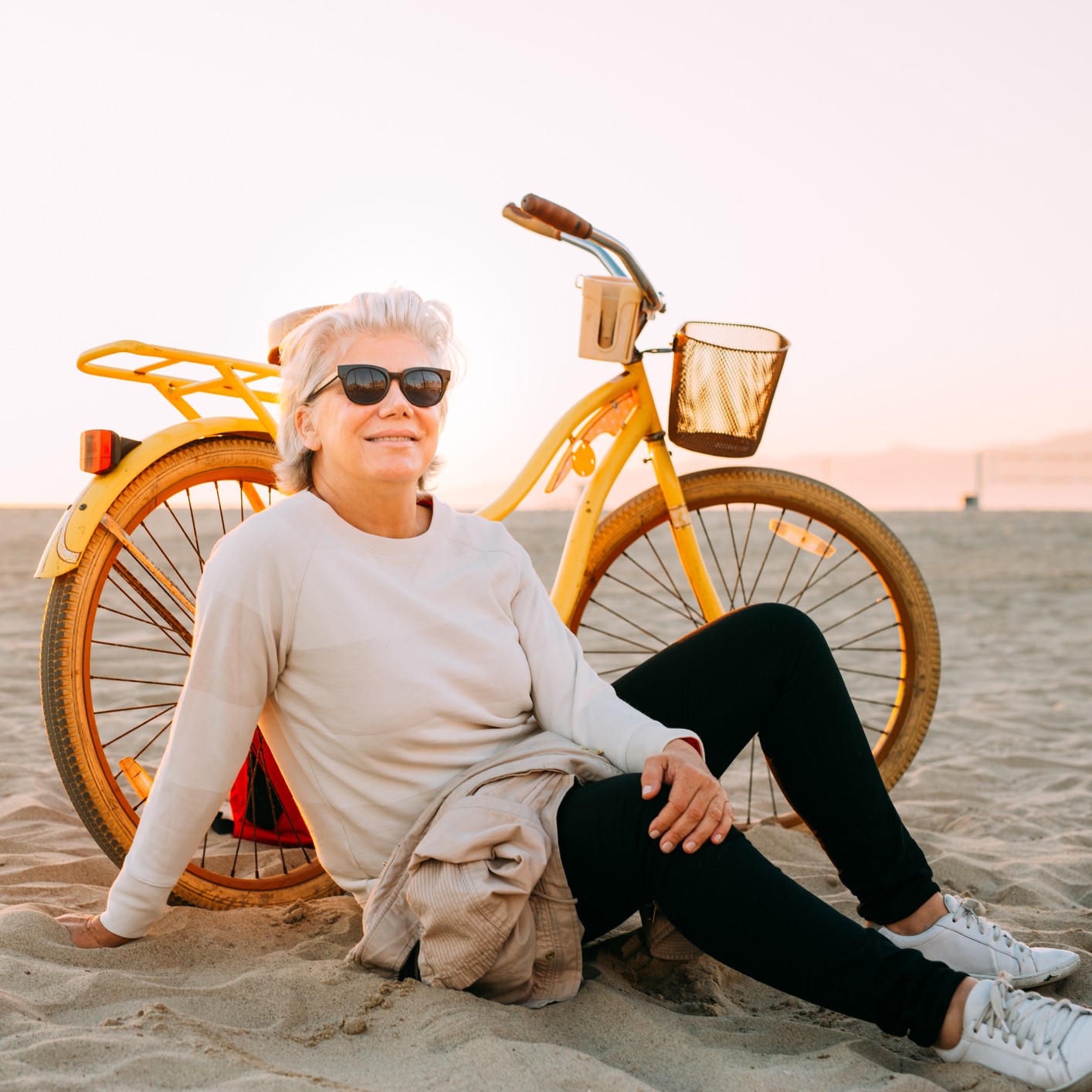 Retired woman sitting on the beach next to bicycle with a basket