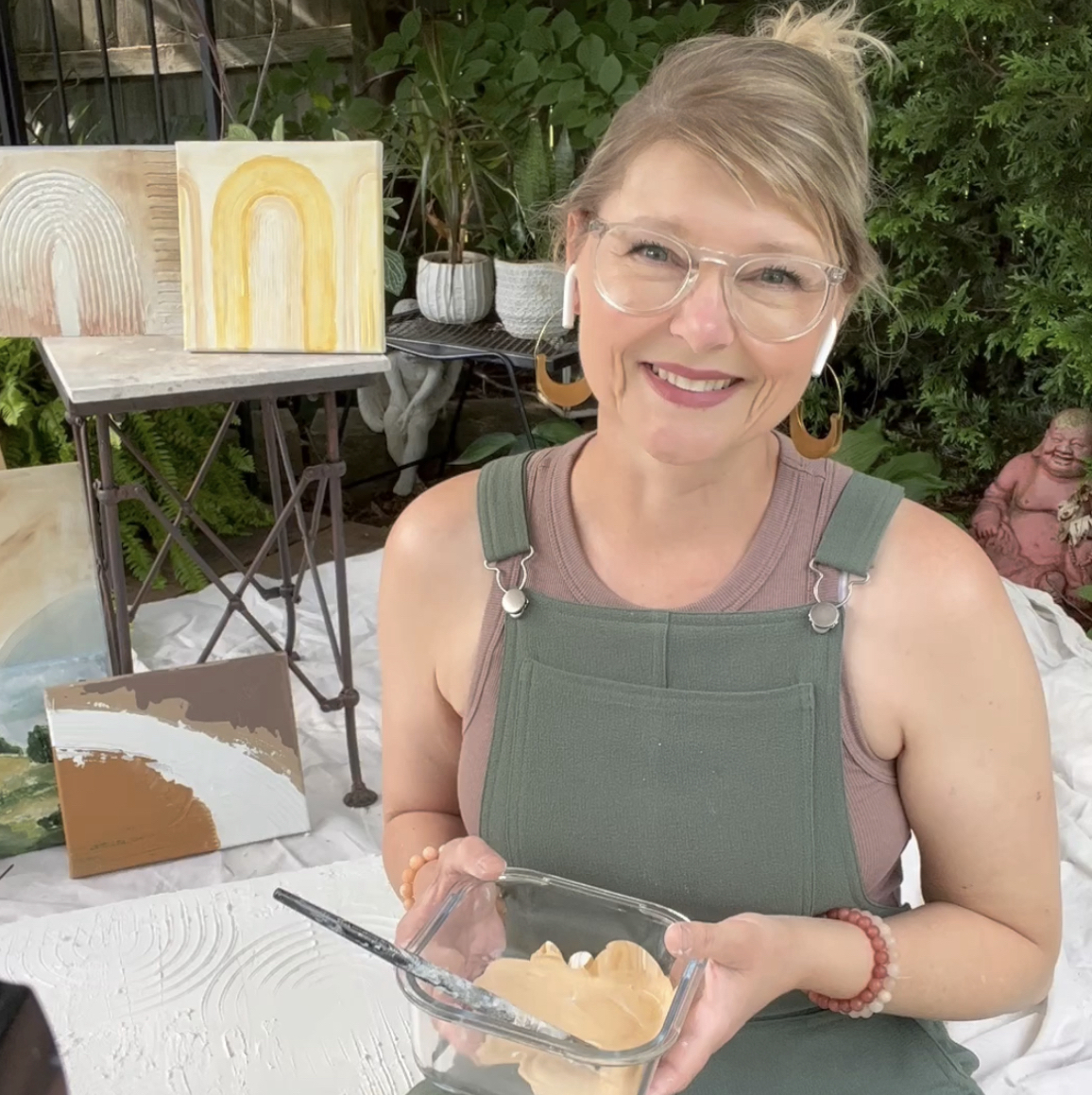 Jennifer Rizzo sitting with art behind her and paint in a dish in her hands