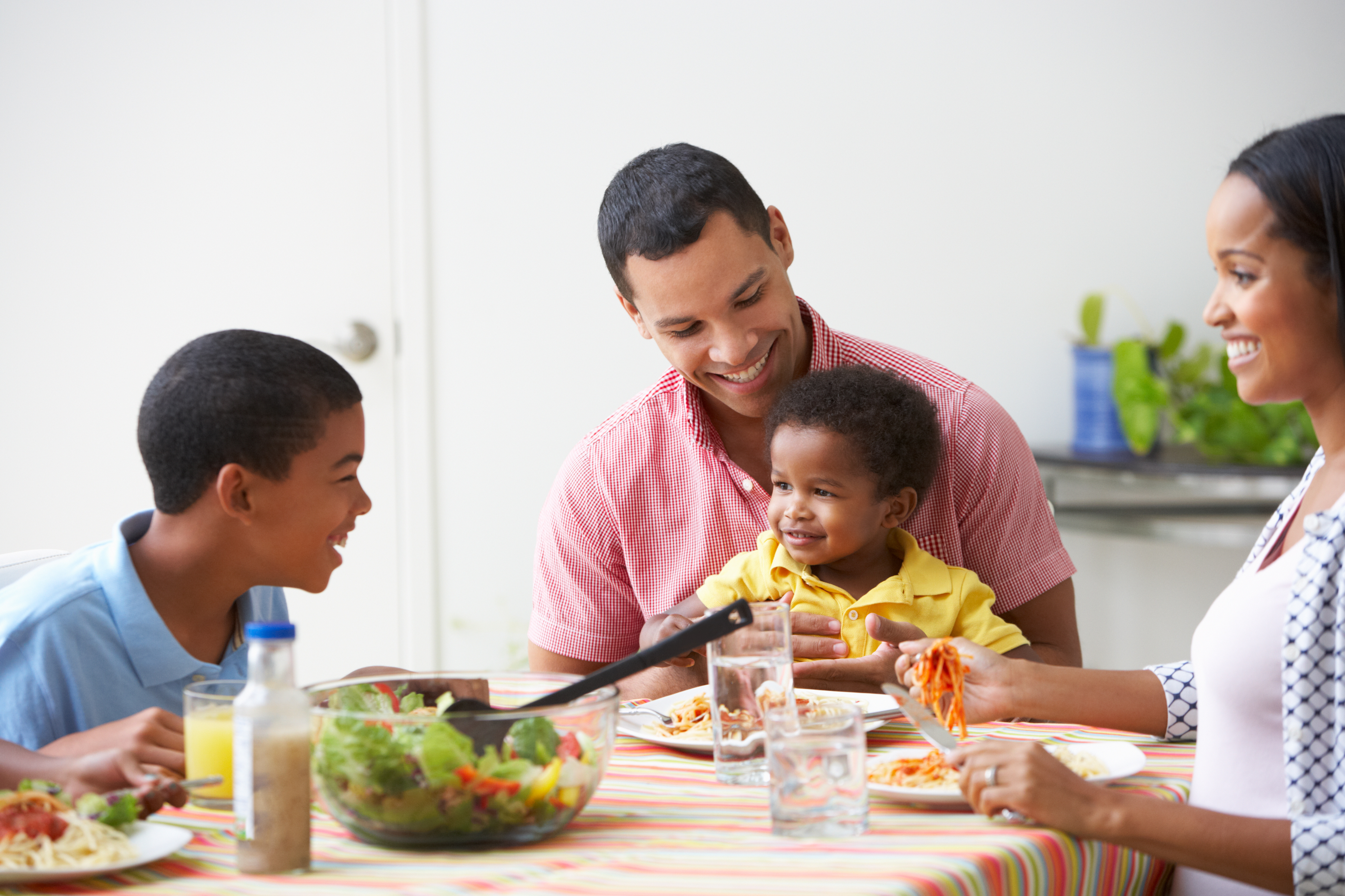A smiling family (Black) eating dinner with two small children