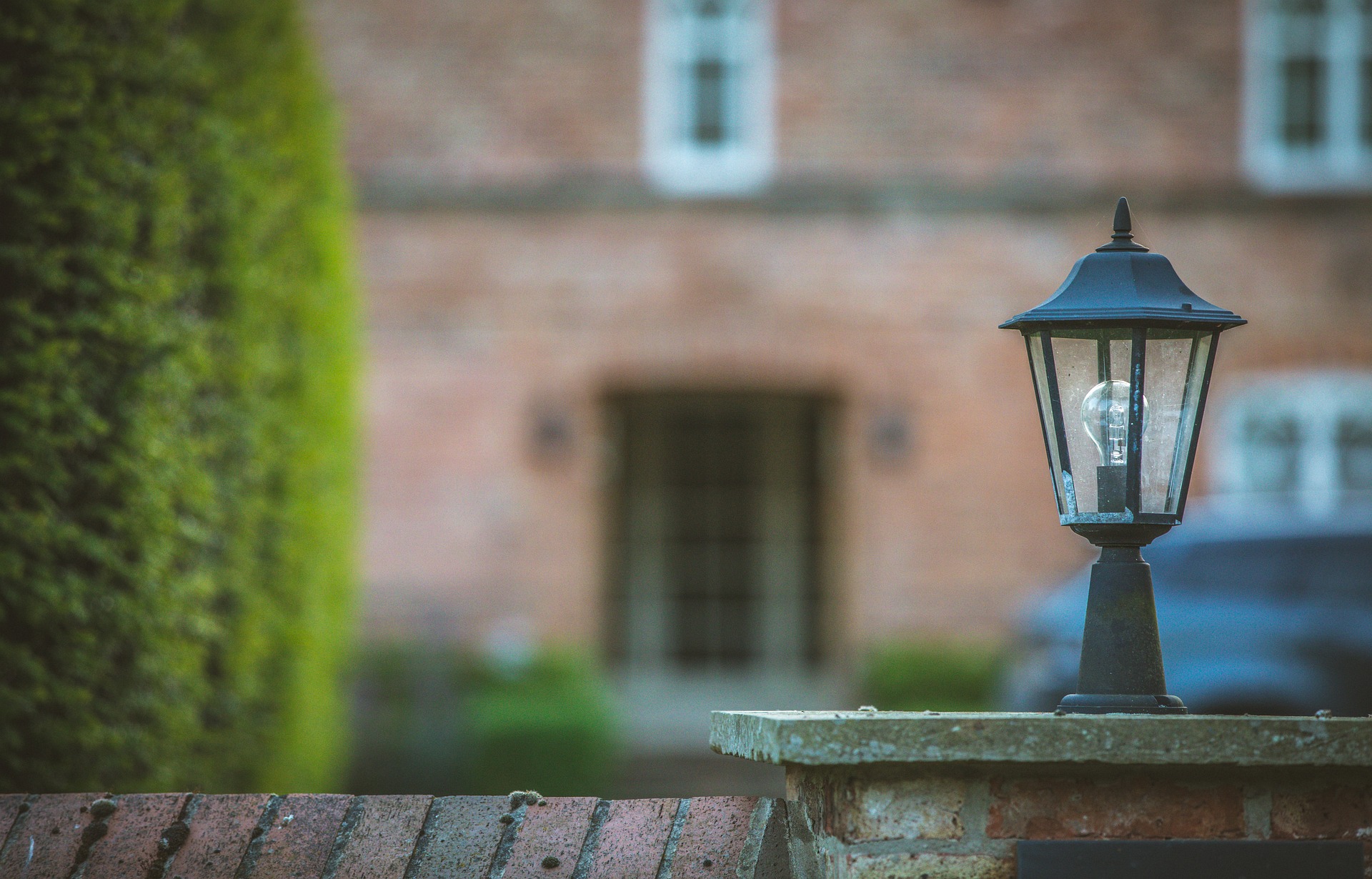 Vintage black lantern on a brick pillar with a blurred red brick building in the background.