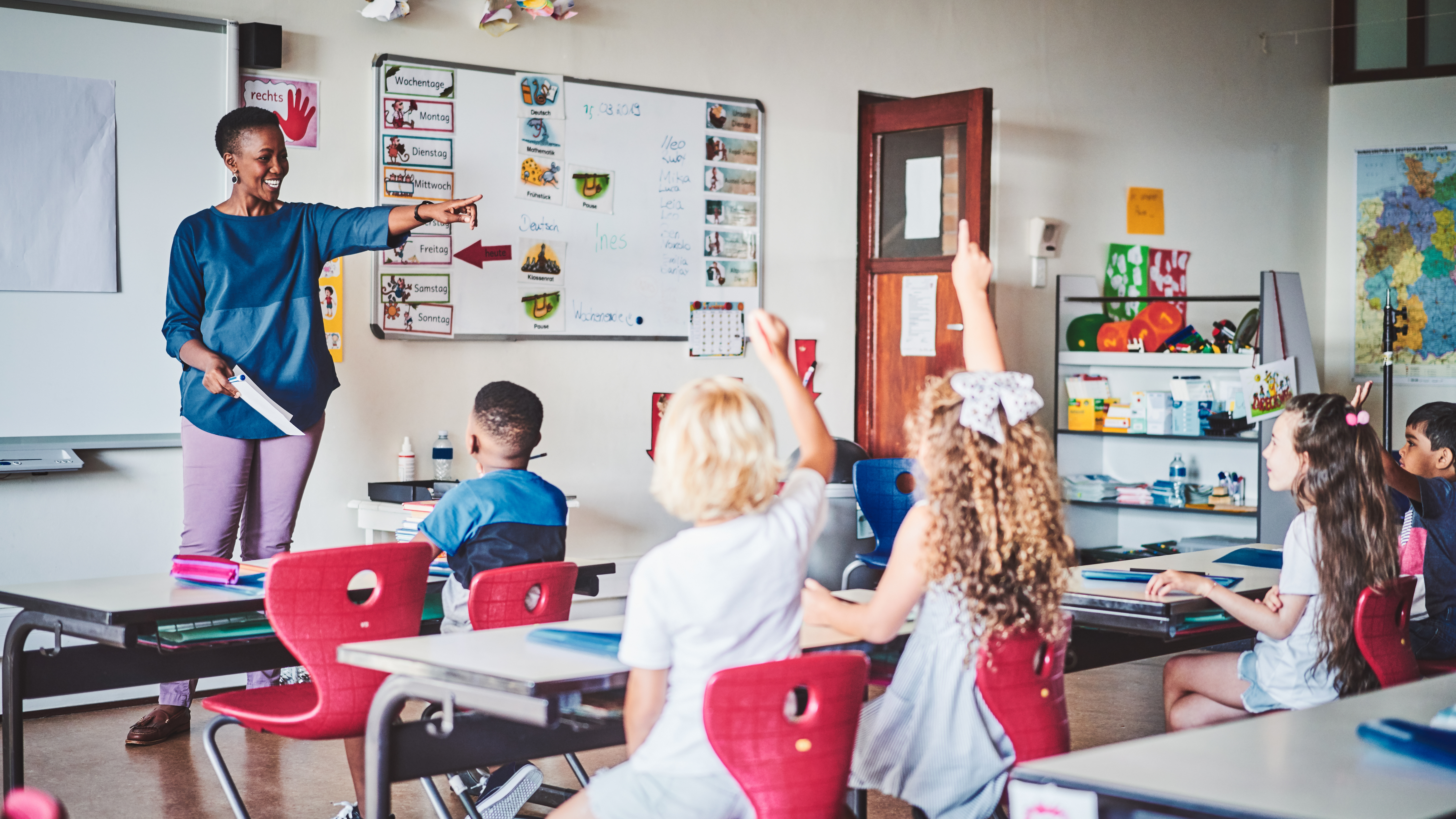 teacher standing in front of classroom calling on students whose hands are raised