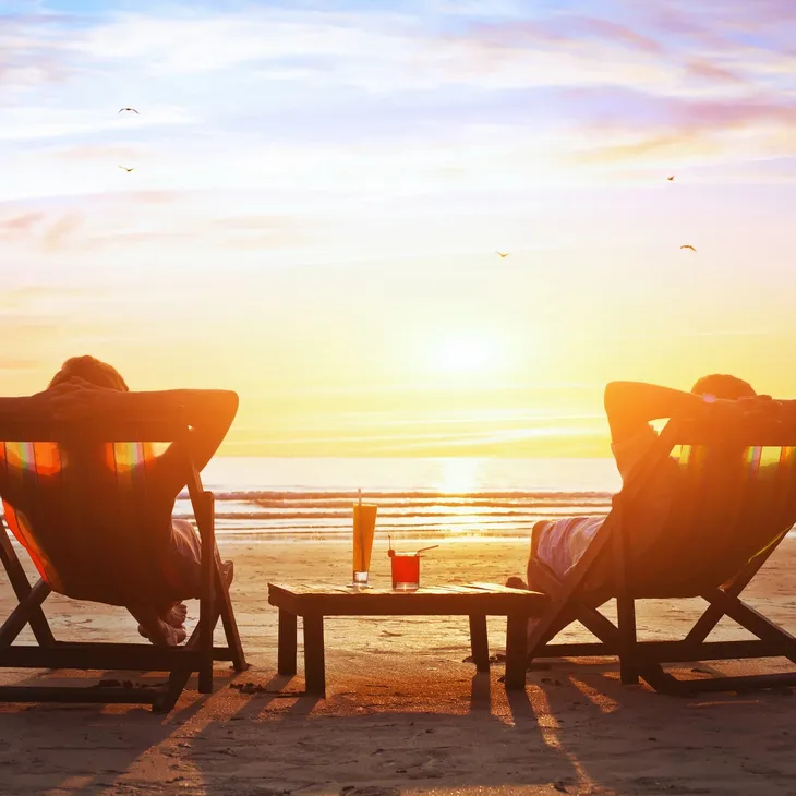 Couple on beach facing ocean sitting in lounge chairs watching sunset